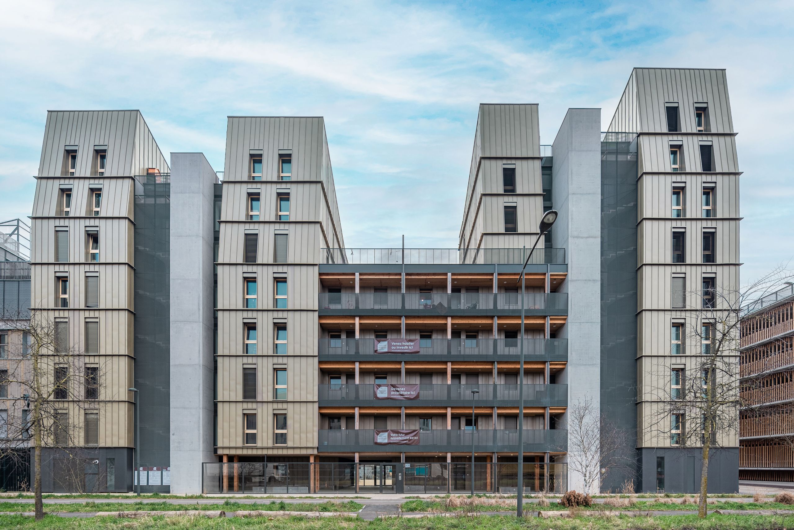Façade de l’immeuble de 98 logements à Strasbourg par Tectoniques, volumes métalliques rythmés, balcons filants en bois et noyaux en béton apparent.