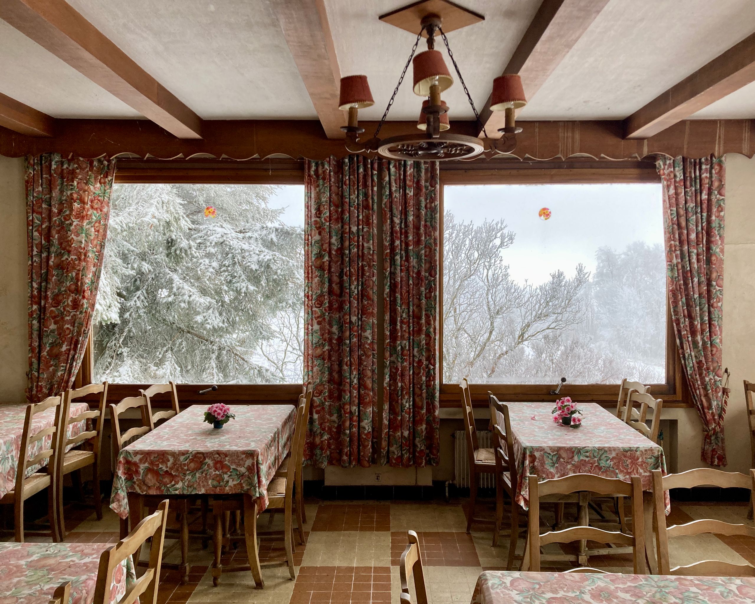 Salle de restauration de l’auberge du col de l’Oeillon à Véranne, boiseries apparentes, grandes baies vitrées sur paysage enneigé, mobilier et textiles fleuris.