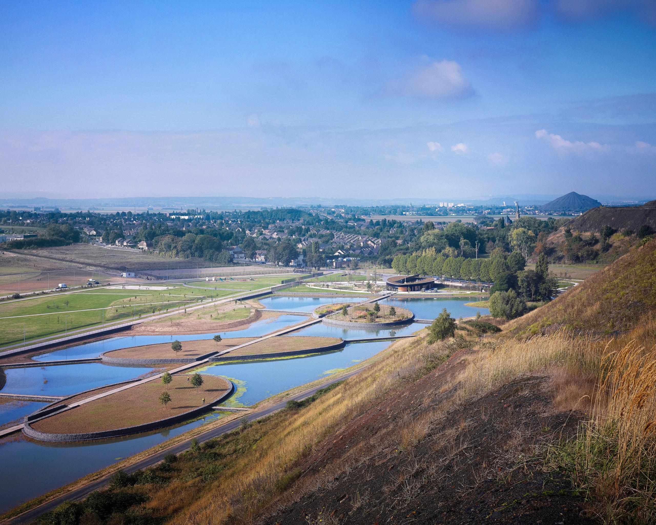 Maison de l’Environnement à Hénin-Beaumont, pavillon ovale en bois et métal au bord des plans d’eau du Parc des Îles, inséré dans le paysage minier reconverti.