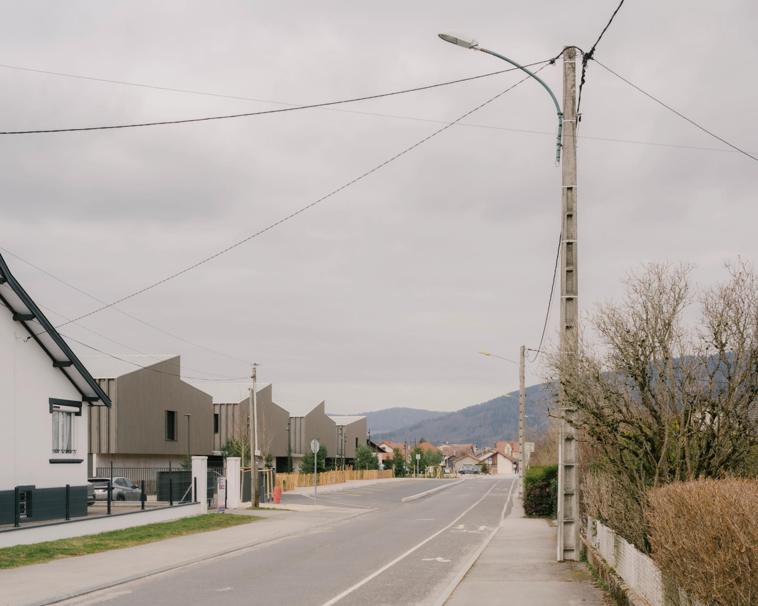 Vue de rue du Collège du Ban à Vagney : volumes en peigne en bois vosgien, pignons rythmés côté pavillonnaire, intégrés au paysage de plaine forestière.