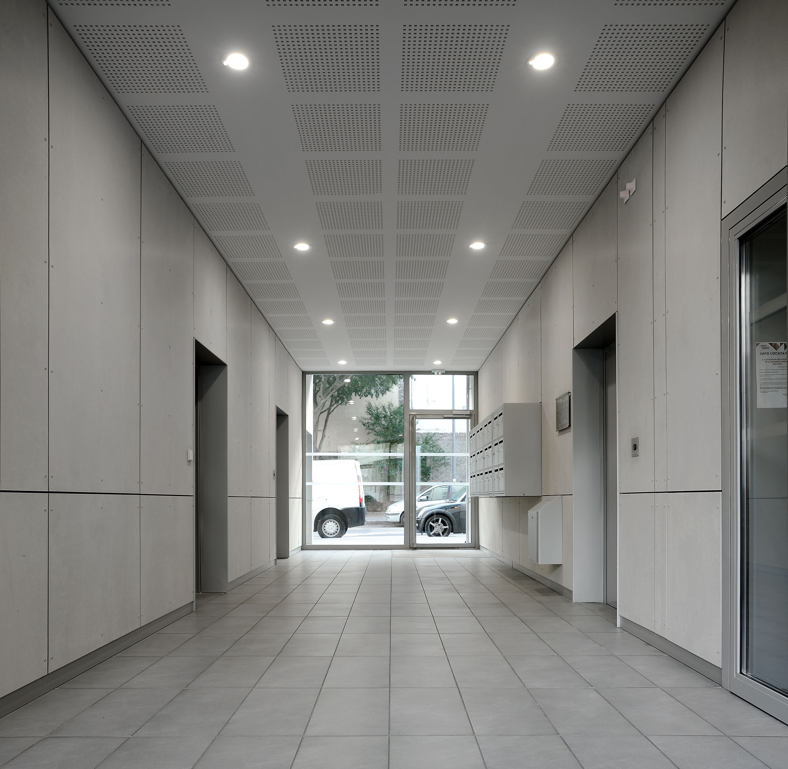 Hall d’entrée des 28 logements à Villeurbanne, traité en volume traversant, murs et plafond clairs, éclairage encastré, boîtes aux lettres et ascenseur en façade latérale.