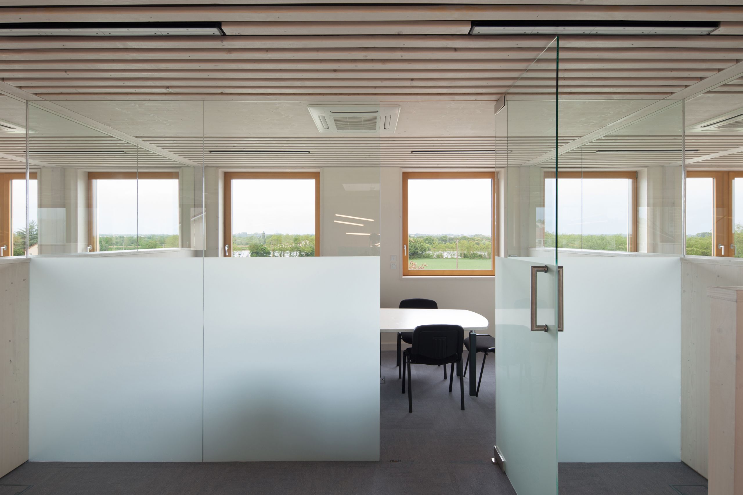 Intérieur du bâtiment tertiaire rénové à Saint-Martin-Belle-Roche, cloison vitrée et menuiseries bois cadrant le paysage, plafond à lames et salle de réunion.
