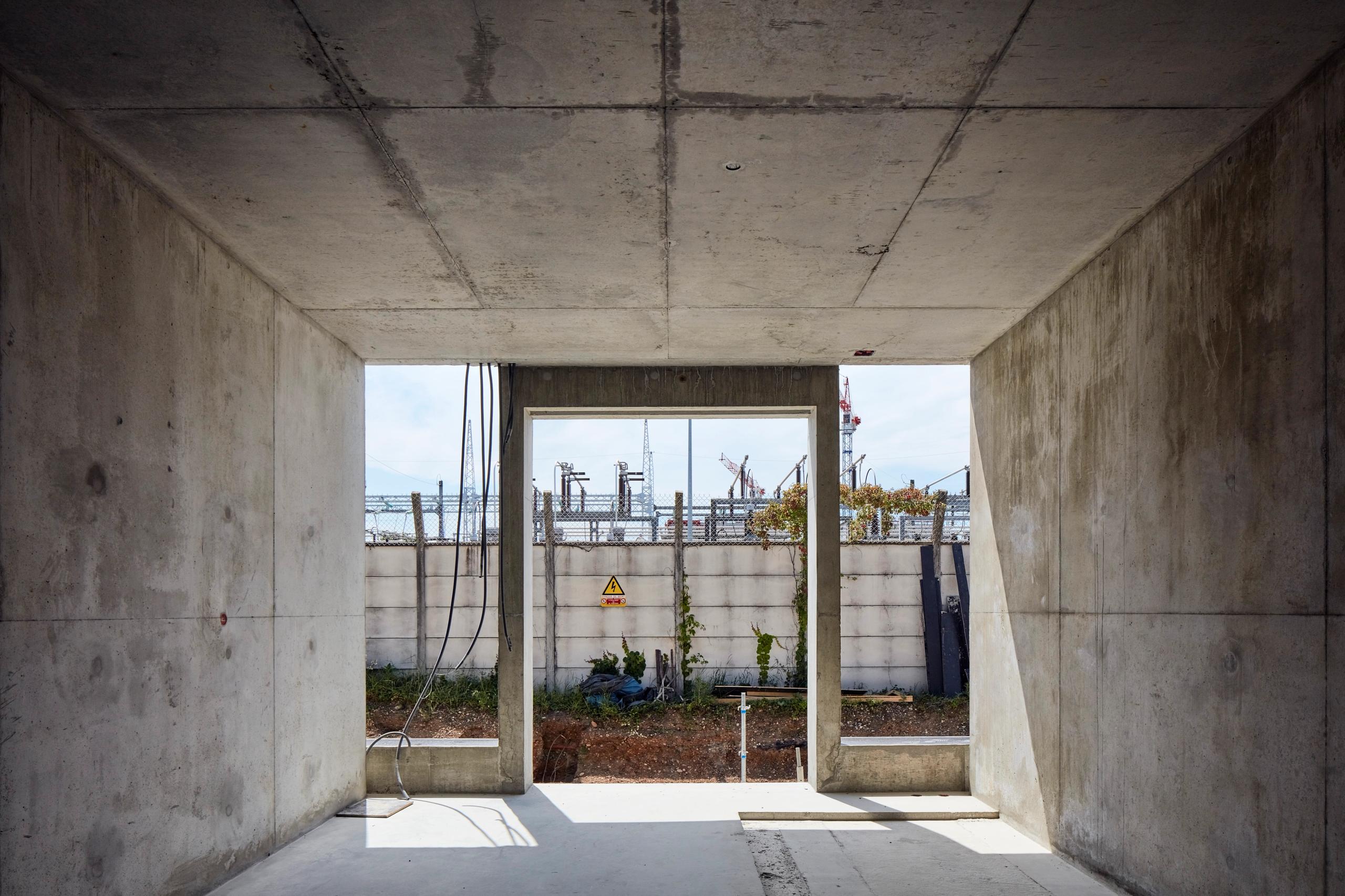 Vue intérieure brute en béton du poste source de Cusset à Villeurbanne, cadrant le paysage industriel extérieur et les équipements électriques voisins.
