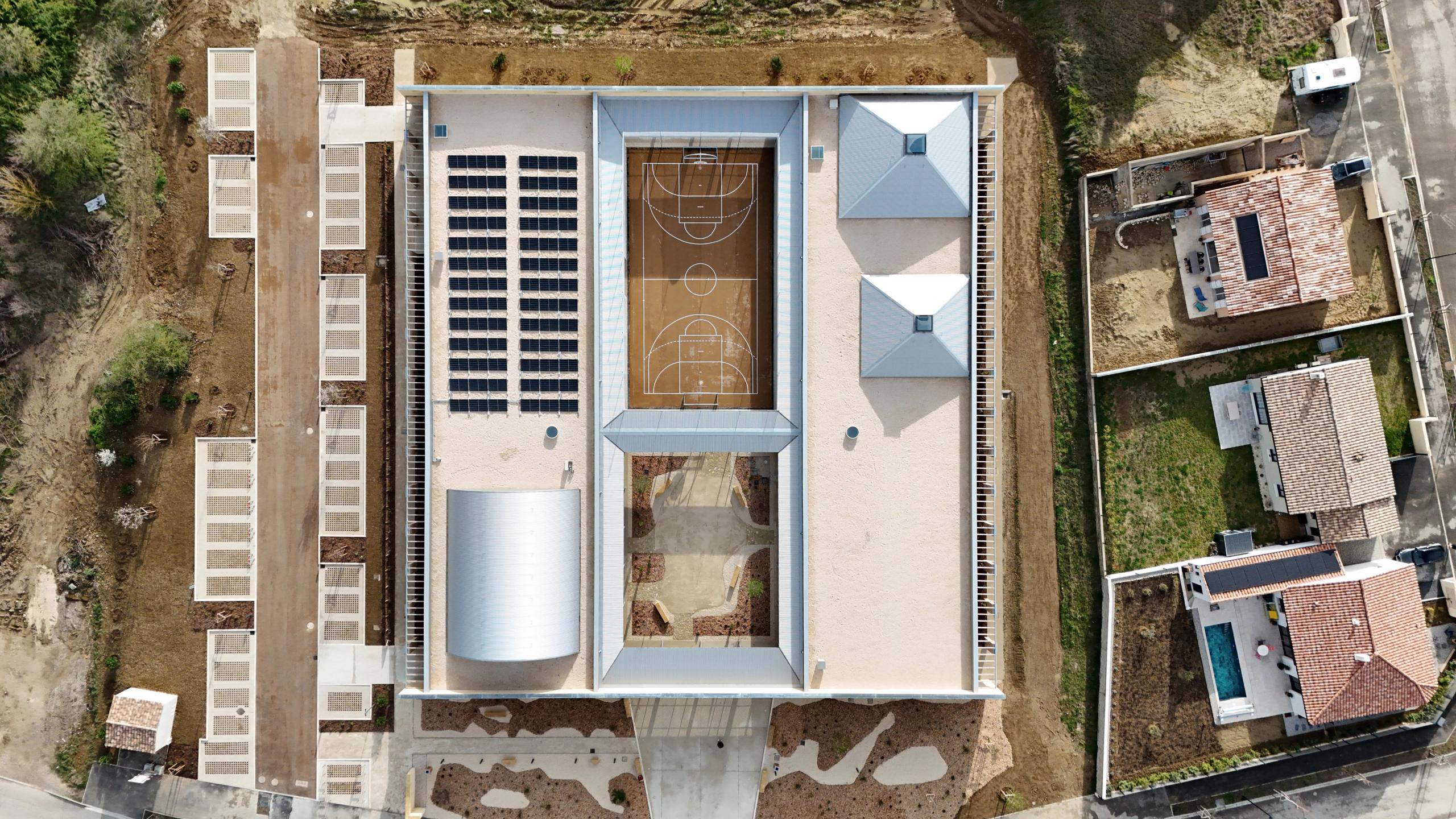 Aerial view of the Youth Cultural Center in Vaison-la-Romaine, a stone-framed courtyard complex with central sports court, garden and solar roofs.