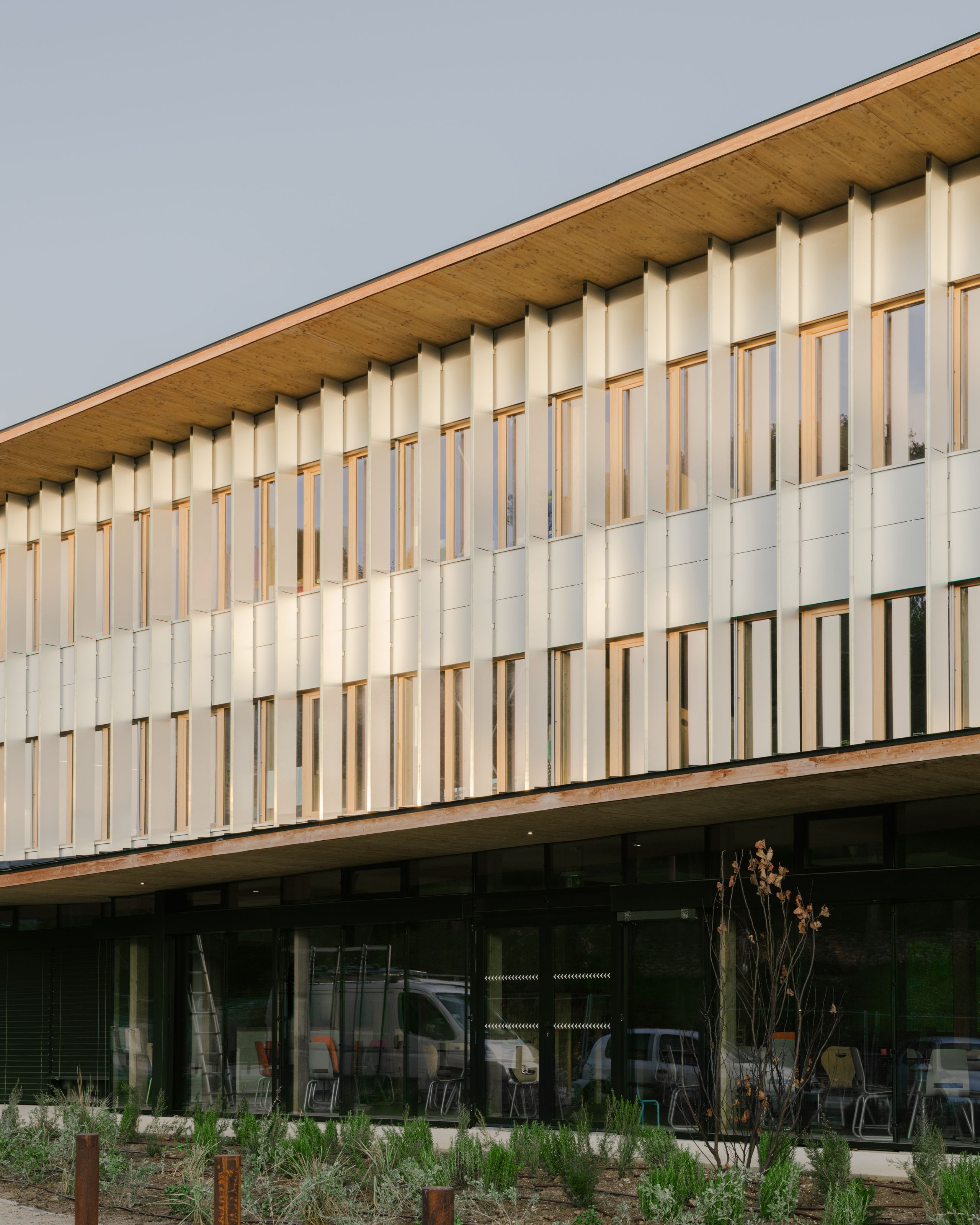 Façade du groupe scolaire Claudie Haigneré aux Pennes-Mirabeau, volume en terrasses à brise-soleil verticaux métalliques et large débord de toiture bois.