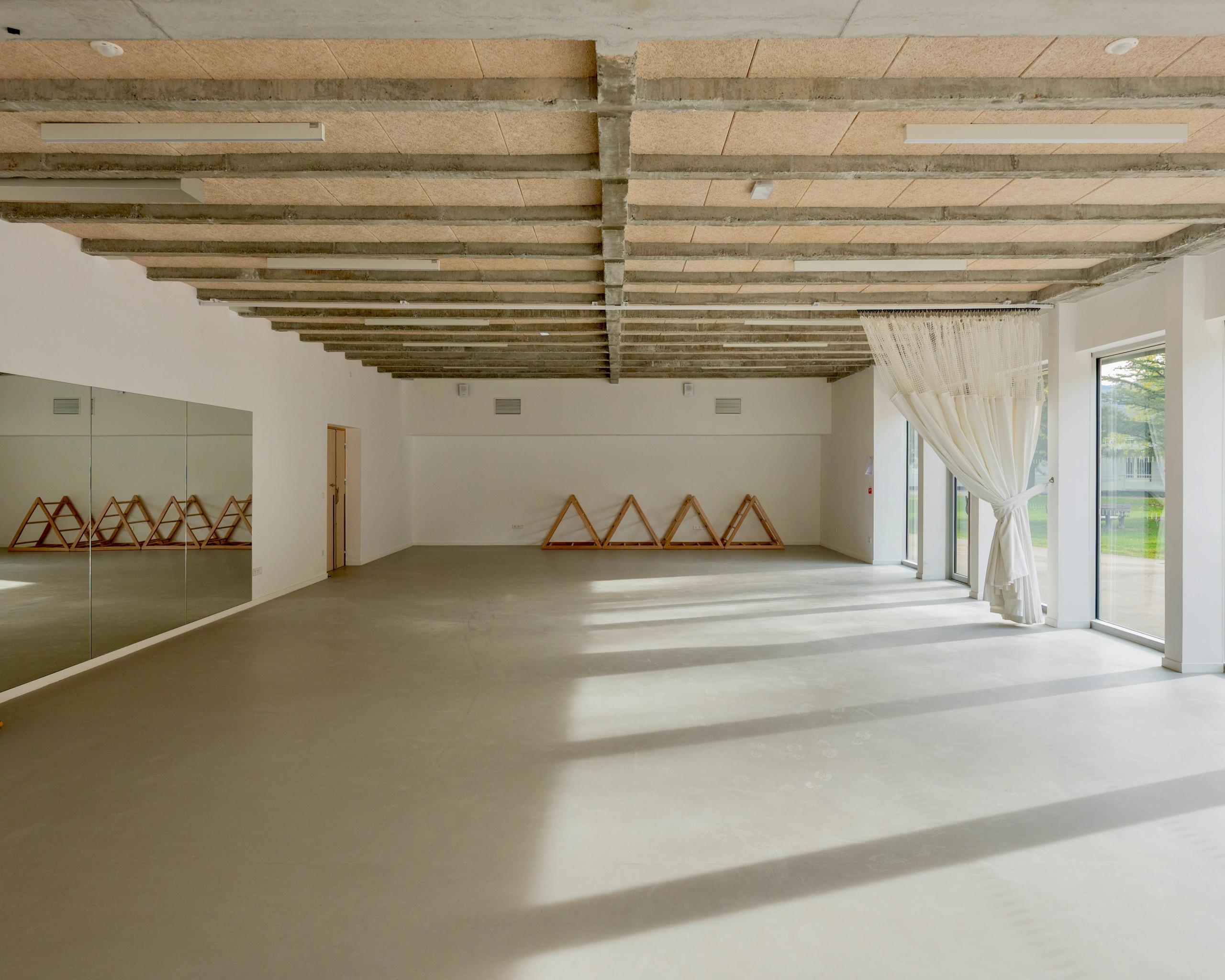 Salle polyvalente du groupe scolaire du Bouchet à Bonneville, structure béton apparente, sol lisse, parois vitrées sur cour et miroirs en paroi latérale.