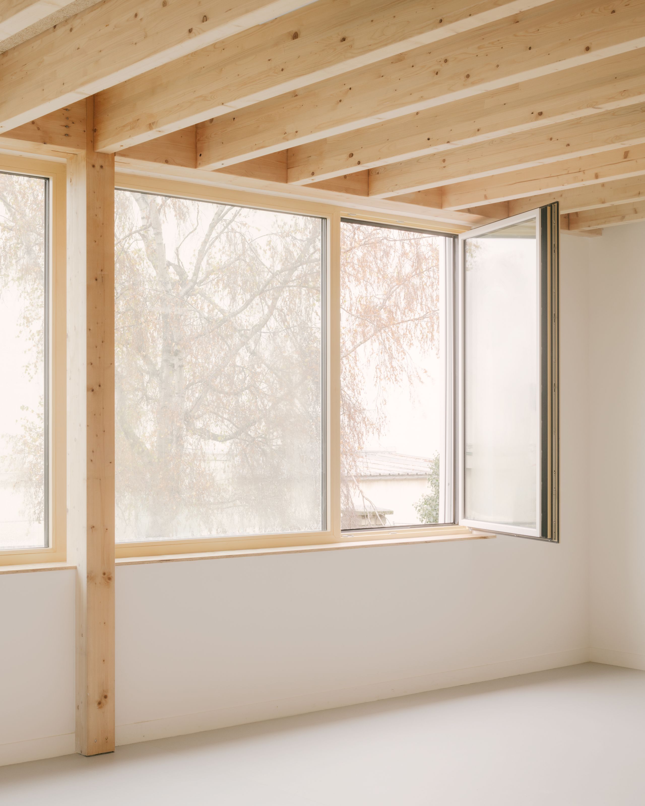Intérieur des groupes scolaires Jacqueline Auriol et Jean Jaurès au Bourget, avec structure bois apparente et large baie vitrée ouvrante sur le parc.