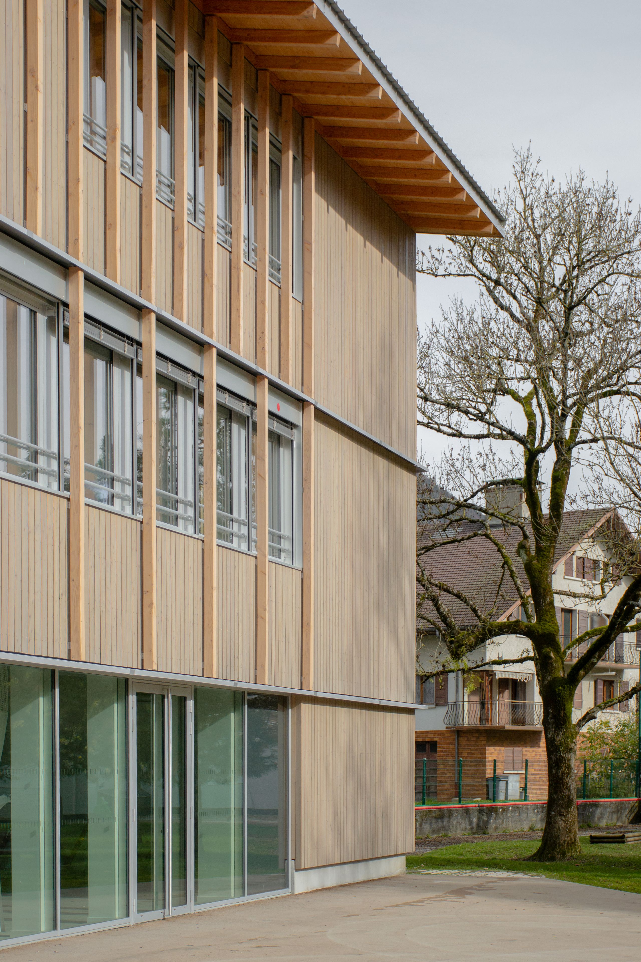 Façade bois et verre du groupe scolaire du Bouchet à Bonneville, surélévation en ossature bois avec grandes baies vitrées ouvrant sur la cour arborée.