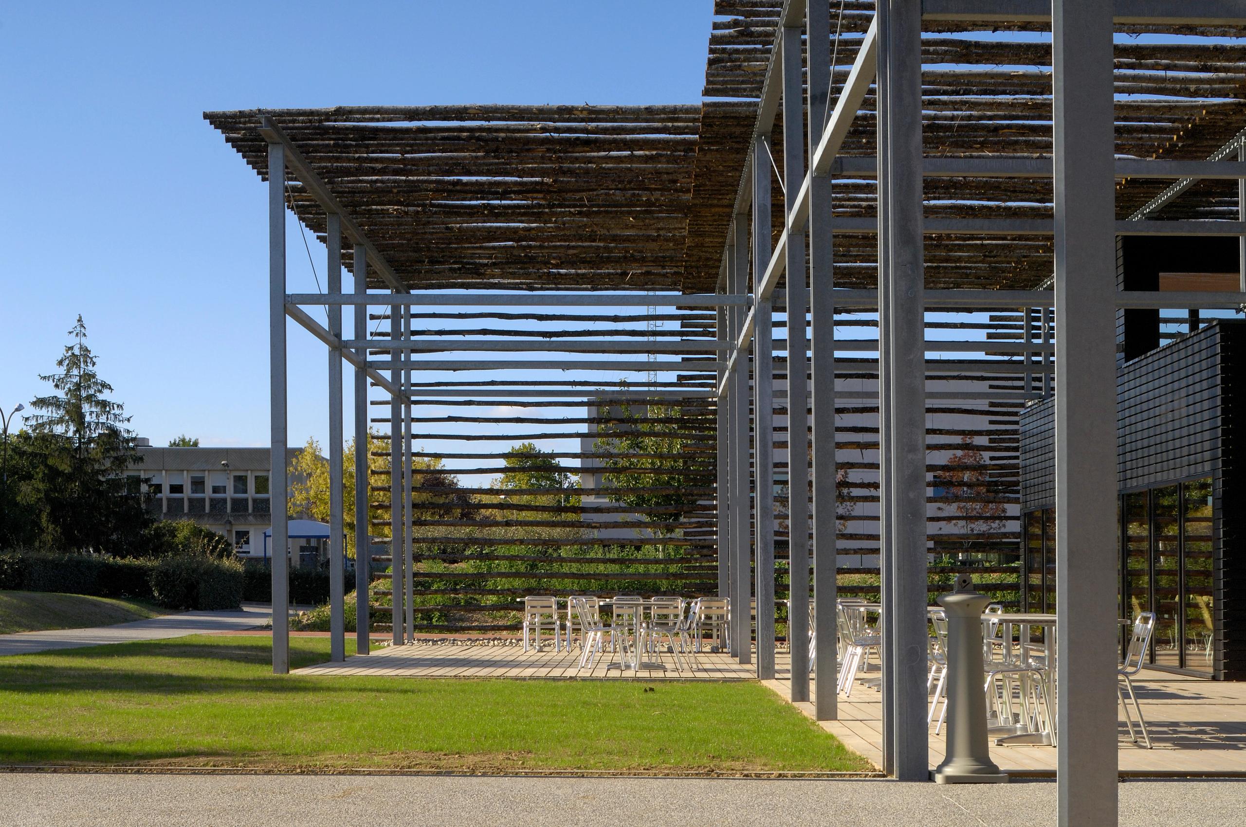 Terrasse du restaurant administratif du CETE à Bron, sous ombrière en baliveaux de châtaignier sur exostructure métallique, ouverte sur le campus paysager.