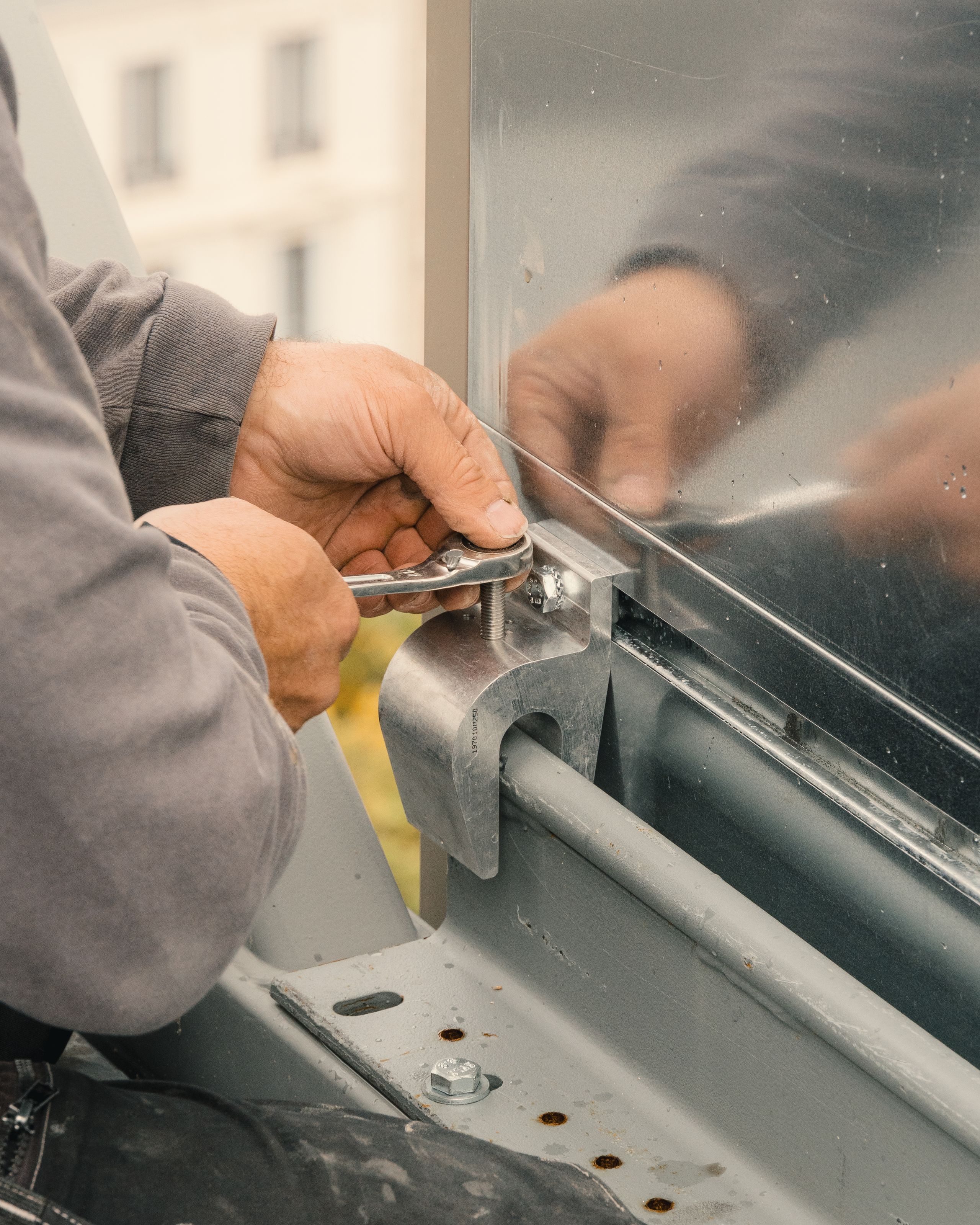 Chantier de réhabilitation de l’IGH Émile Loubet à Saint-Étienne : détail de fixation d’un bardage métallique sur structure acier, serrage manuel d’une platine.