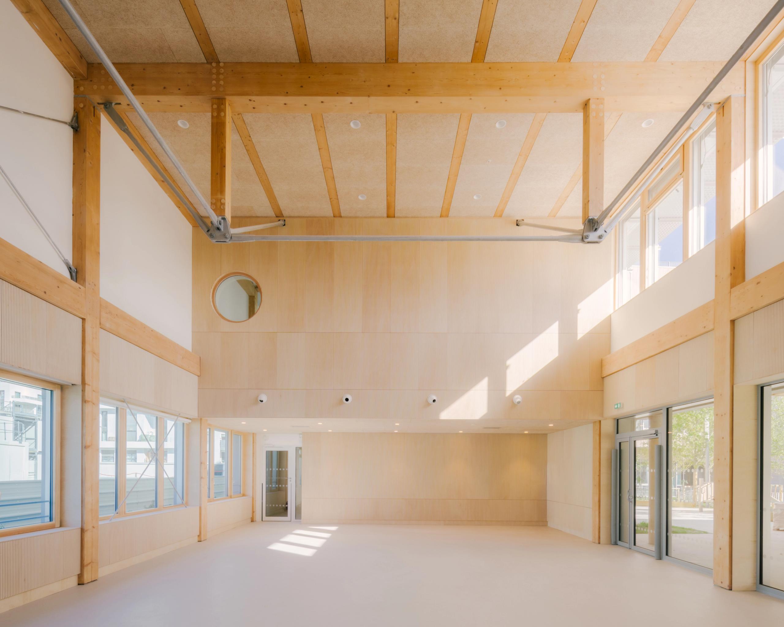 Grand volume intérieur du groupe scolaire Dominique Frelaut à Colombes, structure bois apparente, parois claires, larges baies vitrées et lumière naturelle abondante.