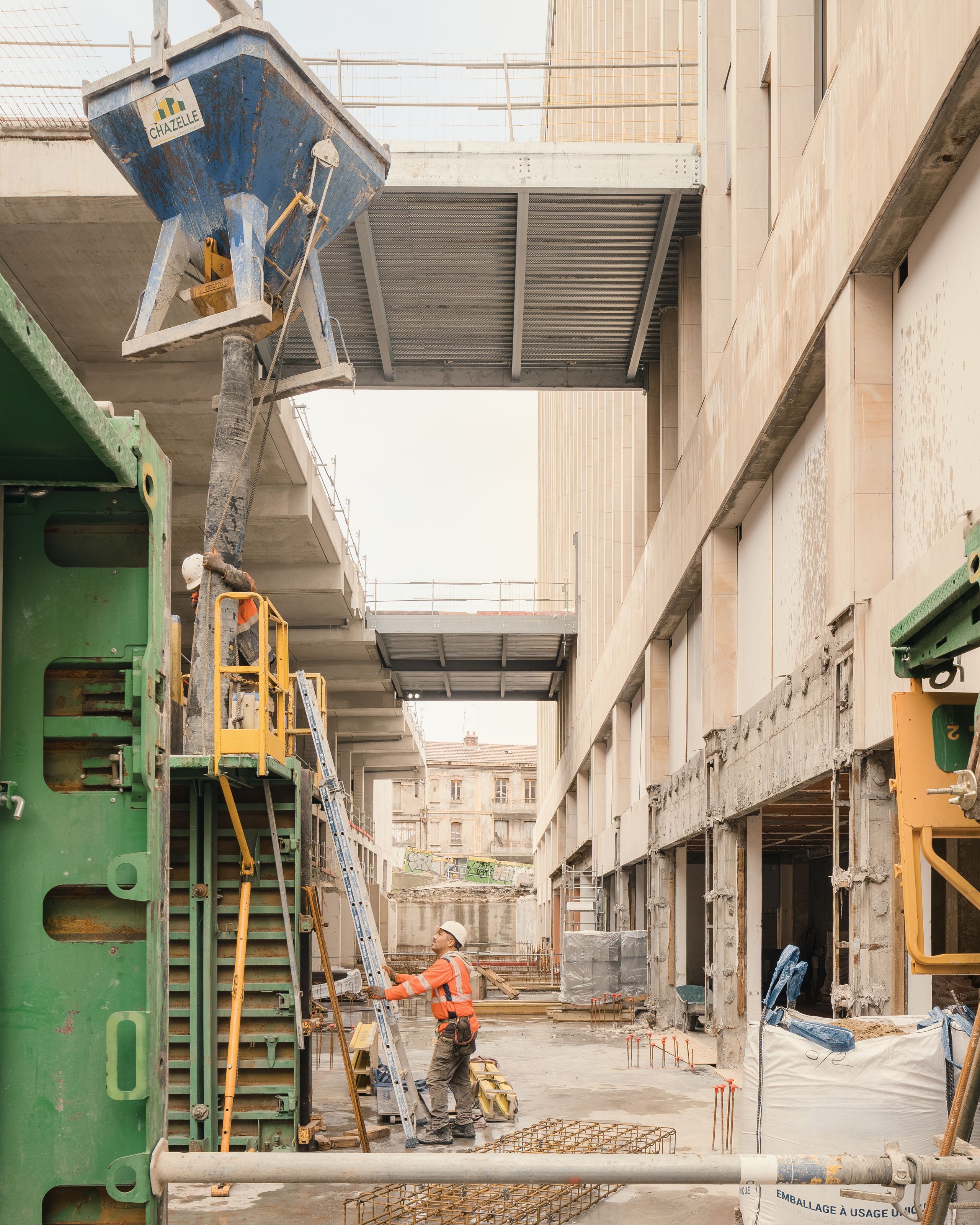 Chantier de réhabilitation de l’IGH Émile Loubet à Saint-Étienne, vue du socle béton curé, façades ouvertes et passerelles métalliques en cours de coulage.