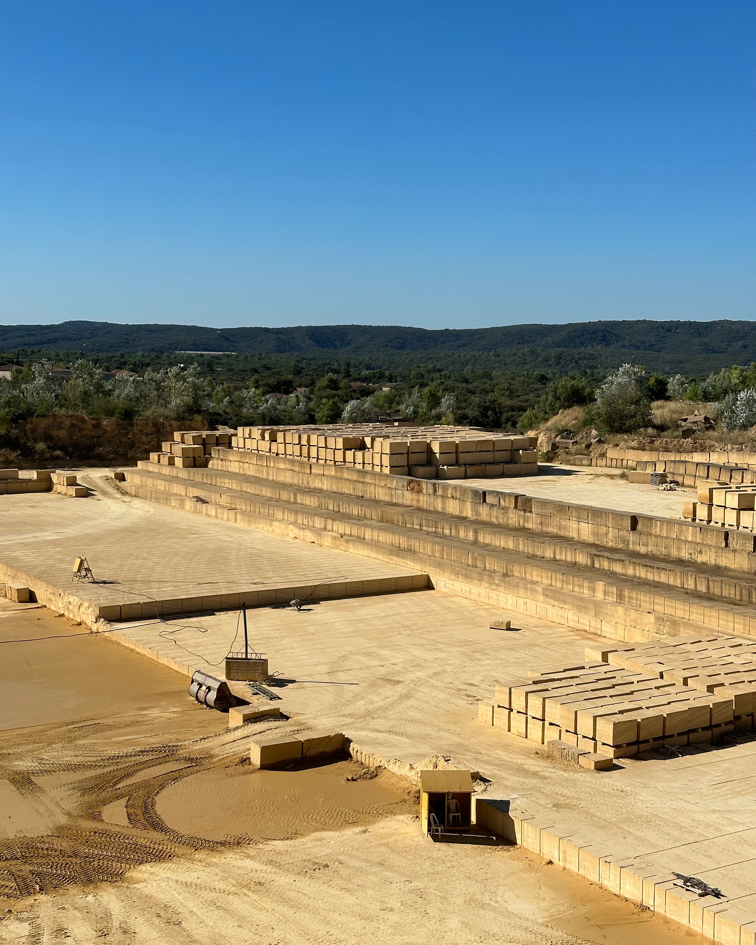 Vue de la carrière de pierre massive à Vaison-la-Romaine, montrant les gradins d’extraction, les blocs calibrés empilés et le paysage naturel en arrière-plan.