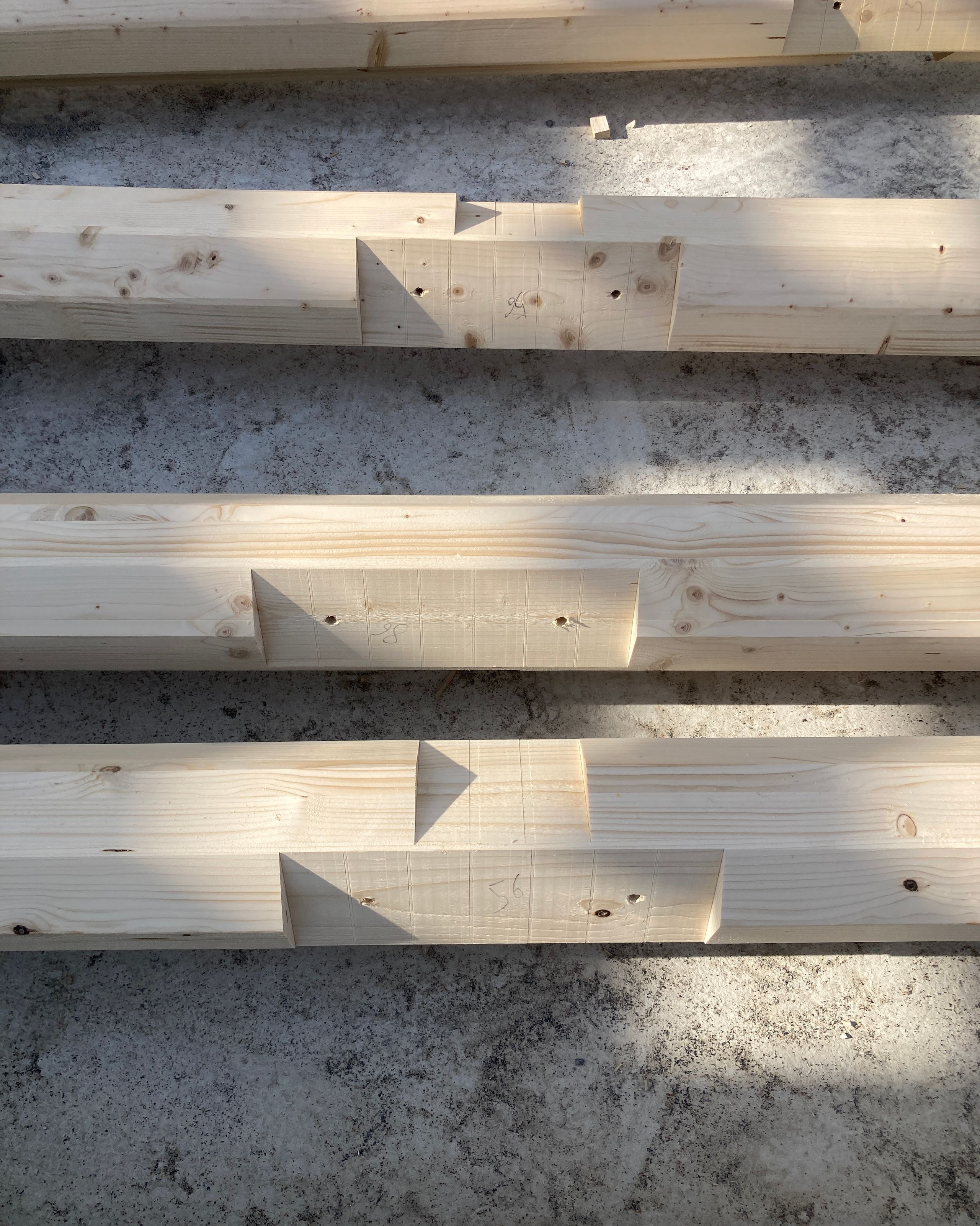 Assemblage de poutres en bois scolyté préfabriquées pour le groupe scolaire Louis Pergaud à Levier, montrant les entailles et repères de charpente.