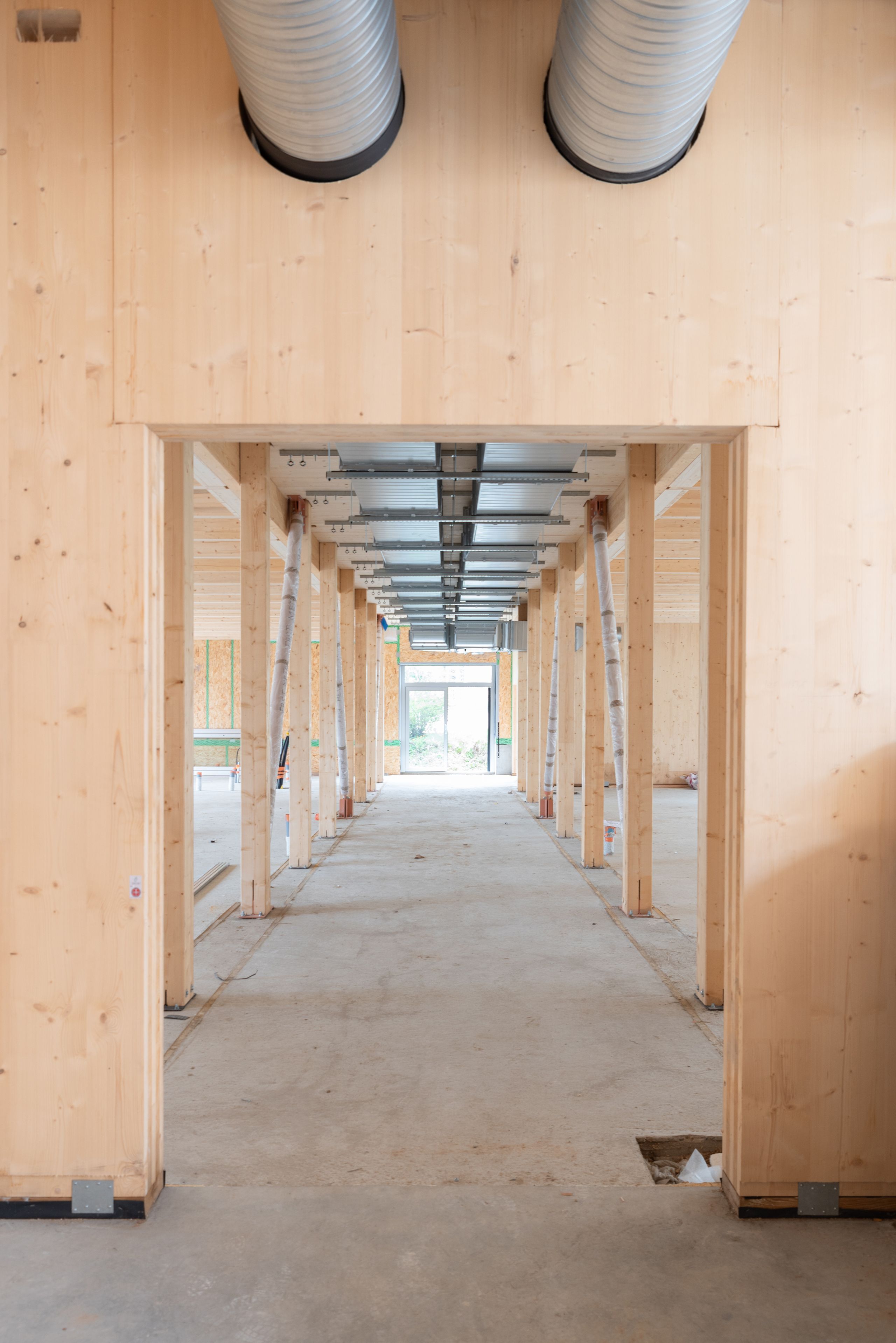 Couloir en structure bois du groupe scolaire Kennedy à Lyon, montrant poteaux, planchers apparents et gaines techniques dans un volume traversant en chantier.