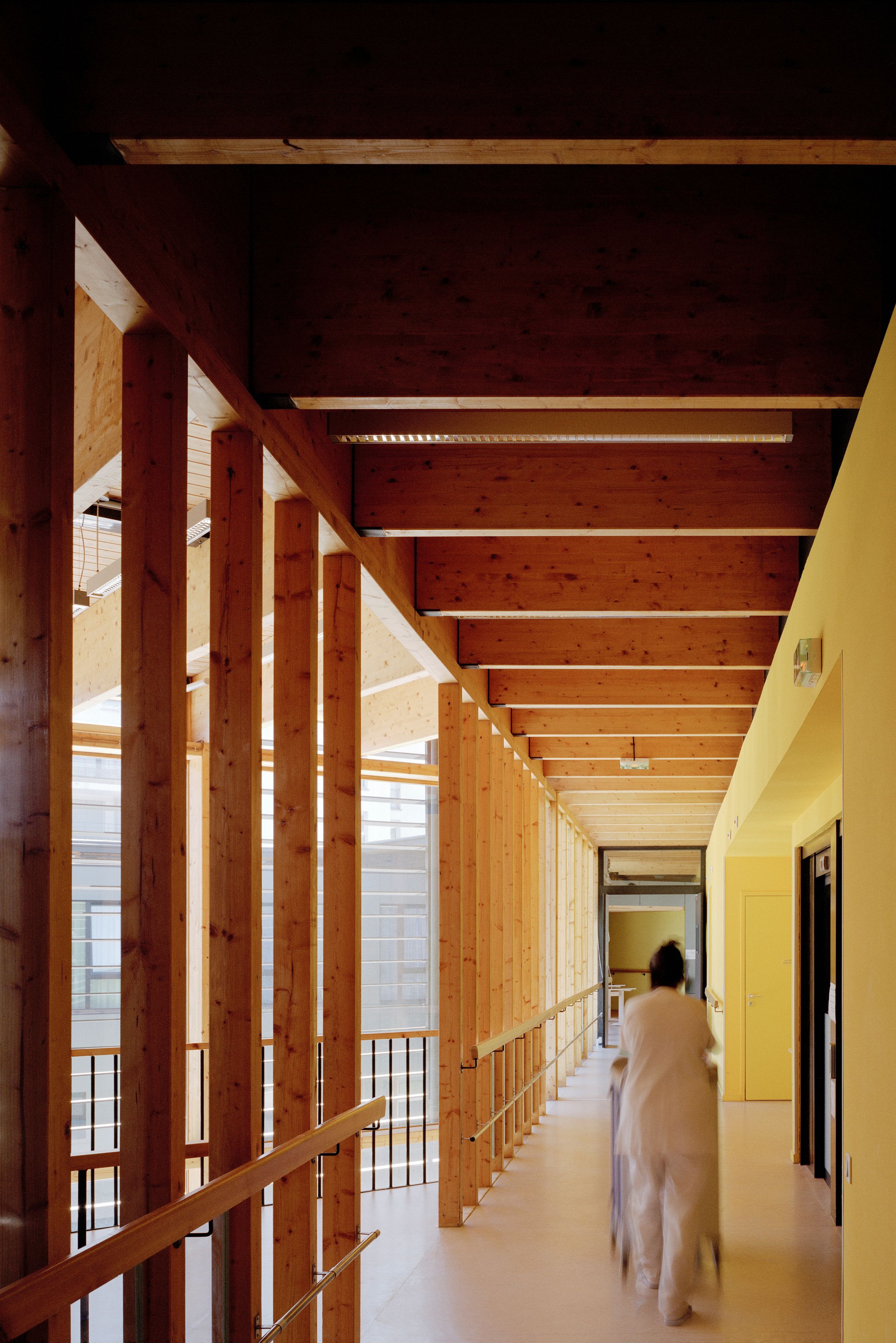 Couloir de l’EHPAD à Grenoble par Tectoniques, structure bois apparente, façade vitrée sur jardin intérieur, lumière naturelle et circulation soignante.