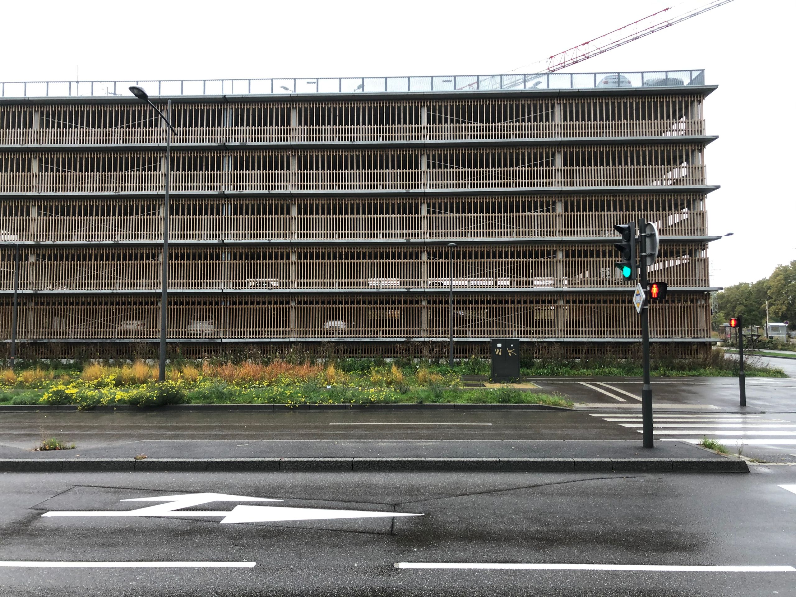 Façade du parking silo Tectoniques à Strasbourg, structure horizontale à lames verticales, niveaux ouverts sur rue et parvis planté en premier plan.