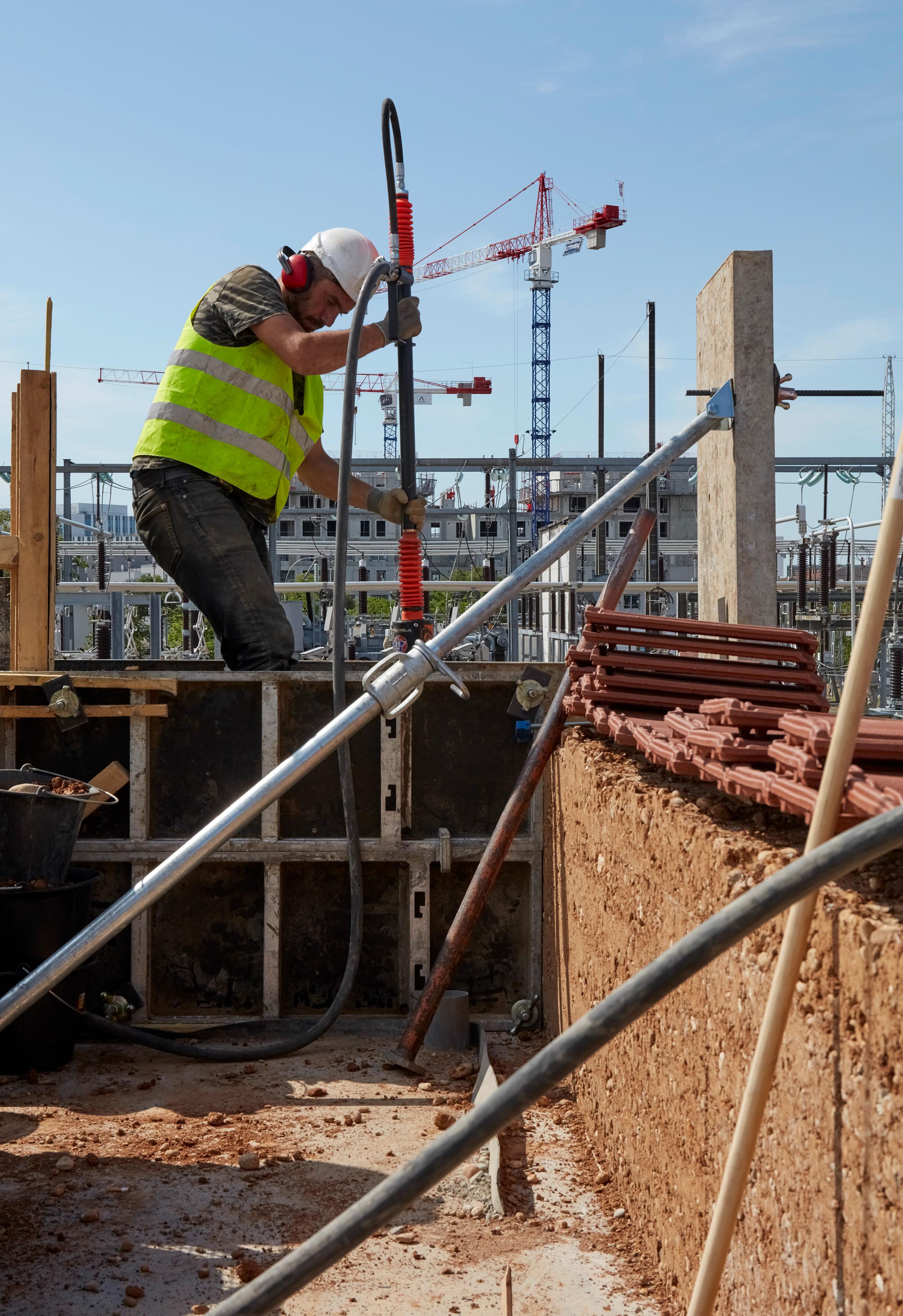 Chantier du poste source de Cusset à Villeurbanne : mur en pisé en cours de mise en œuvre, structure béton-acier apparente et équipements électriques en arrière-plan.