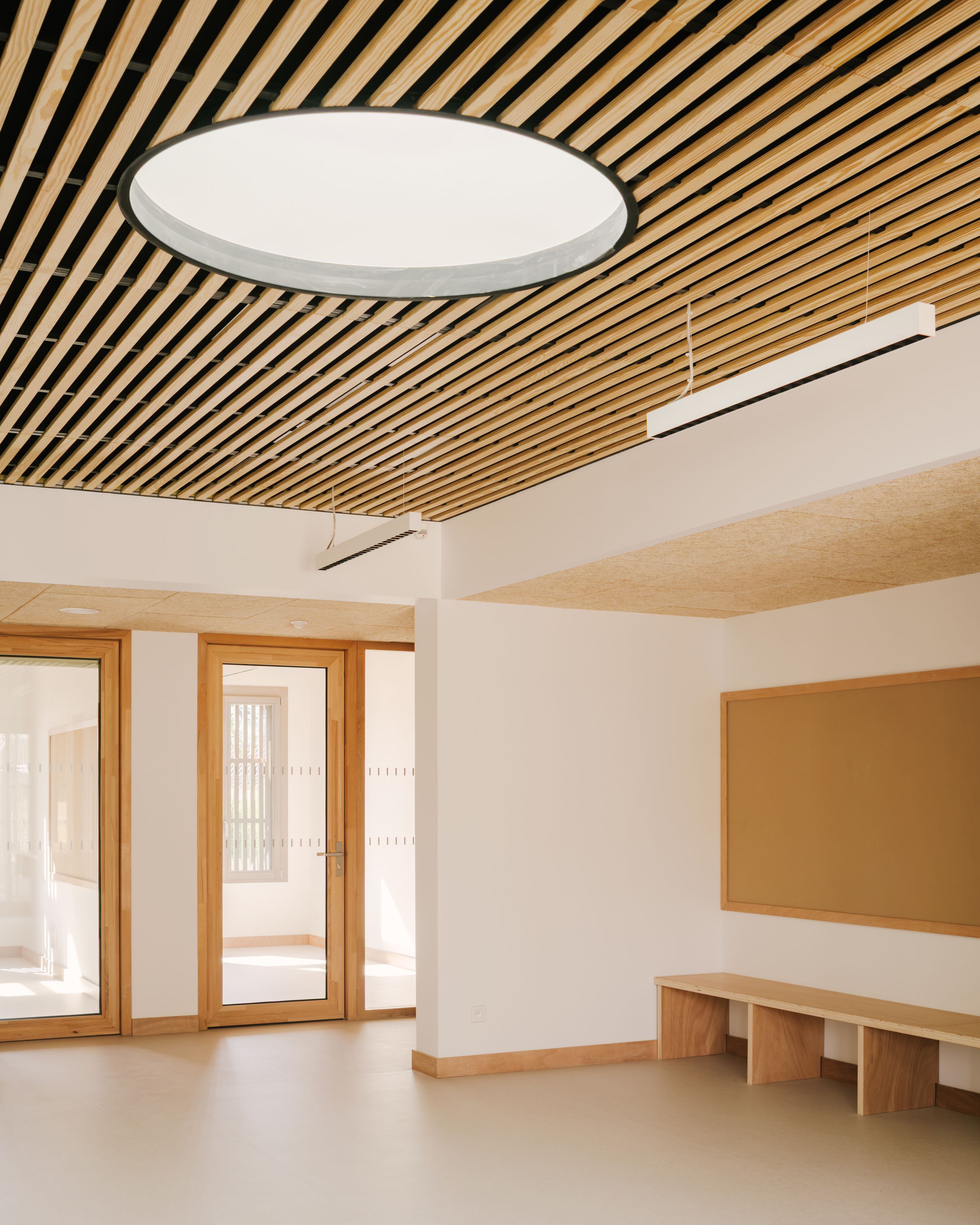 Intérieur du pôle culture et jeunesse à Vaison-la-Romaine, hall lumineux avec plafond à lames bois, oculus circulaire, menuiseries vitrées et mobilier intégré.