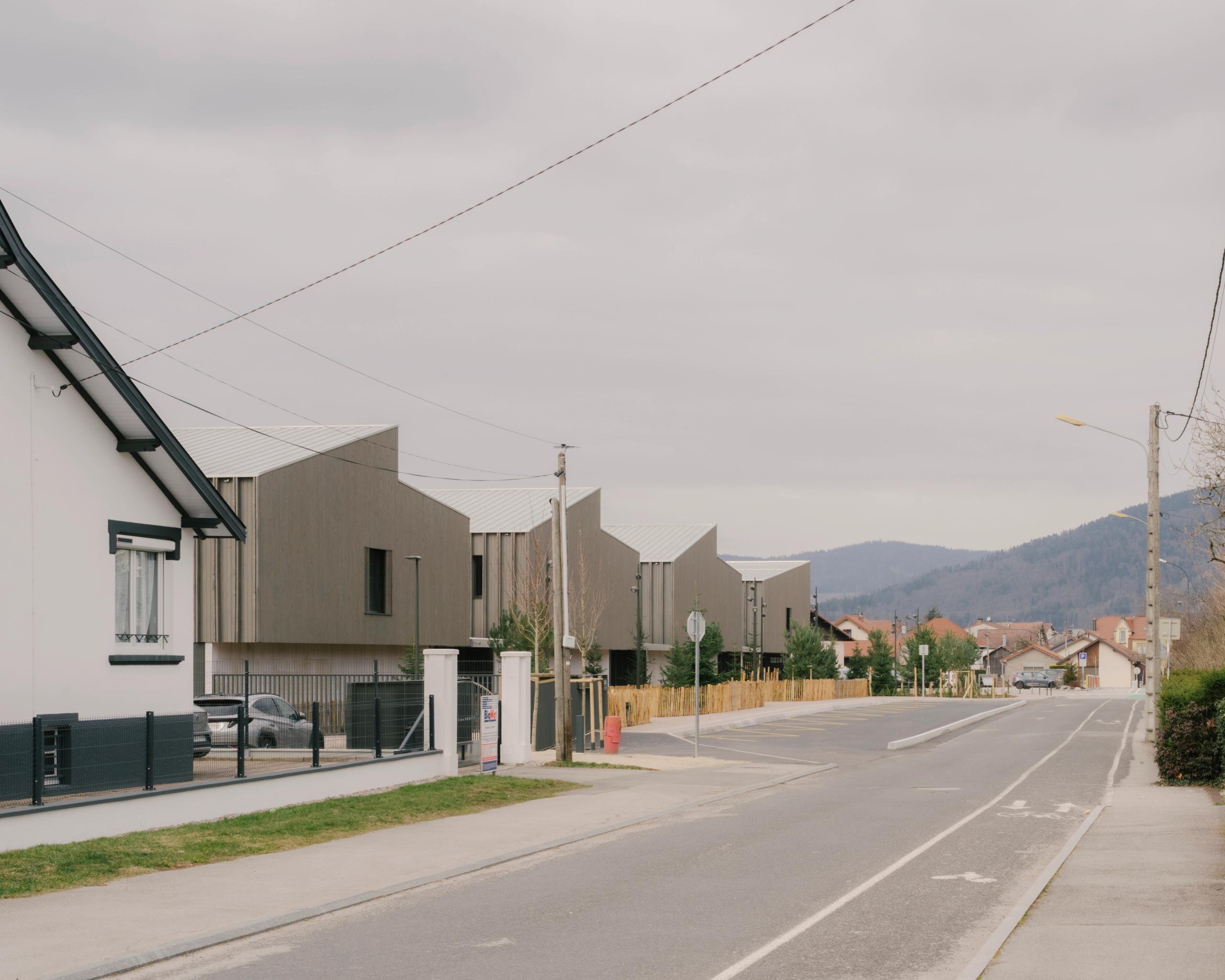 Vue de rue du Collège du Ban à Vagney : ailes en peigne à toitures à deux pans, façades bois vosgien, pignons rythmant le front bâti pavillonnaire.