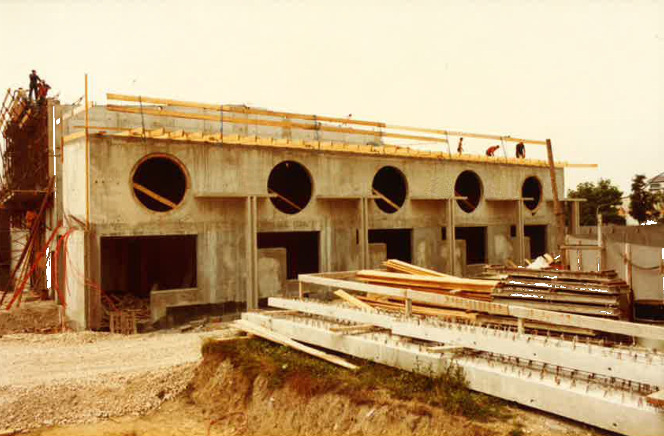 Chantier du conservatoire intercommunal d’Annemasse dans les années 80 : façade en béton brut rythmée par des baies circulaires et rectangulaires.