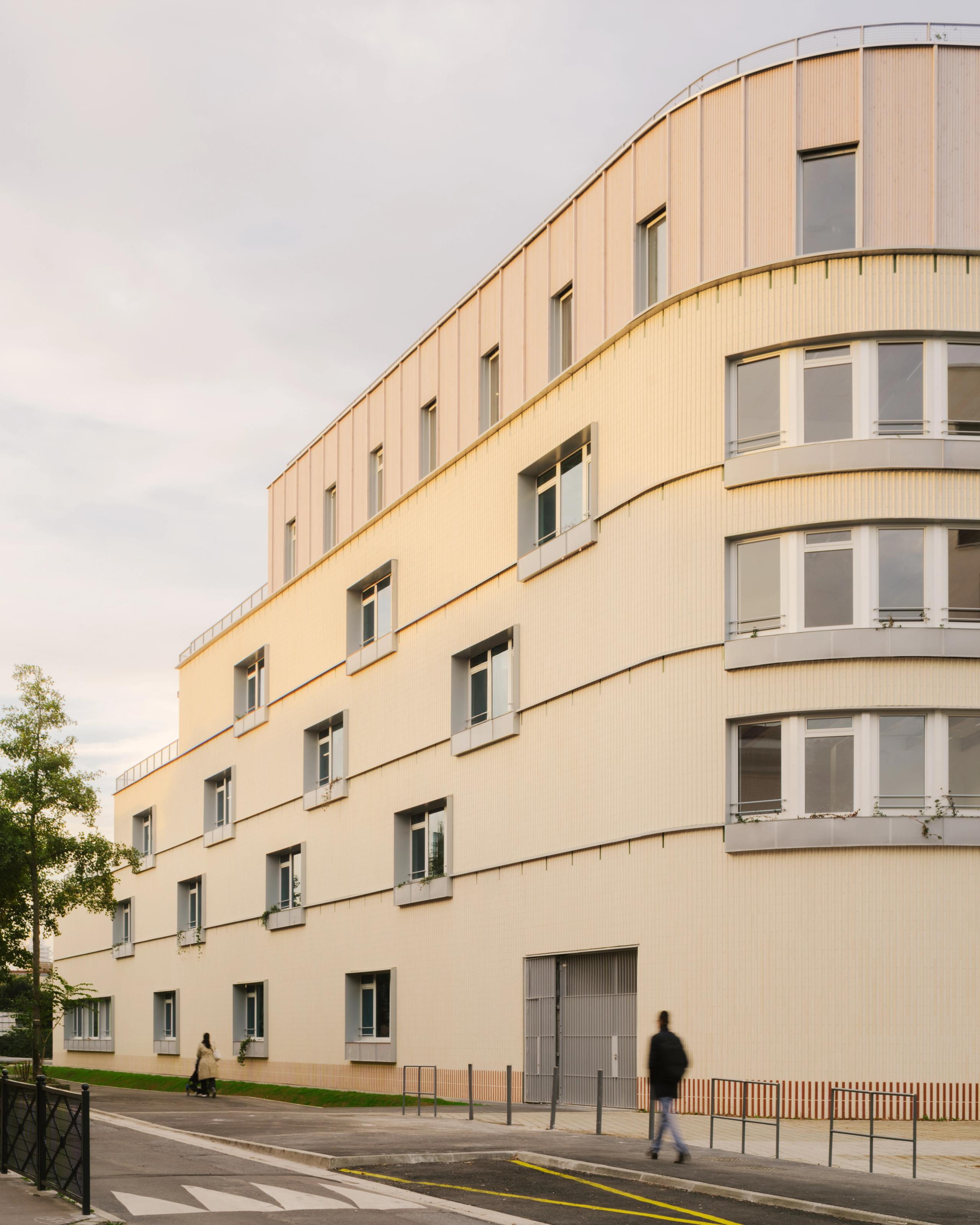 Façade urbaine du groupe scolaire Dominique Frelaut à Colombes, volume courbe en gradins, parement clair rythmé de baies régulières et socle minéral.