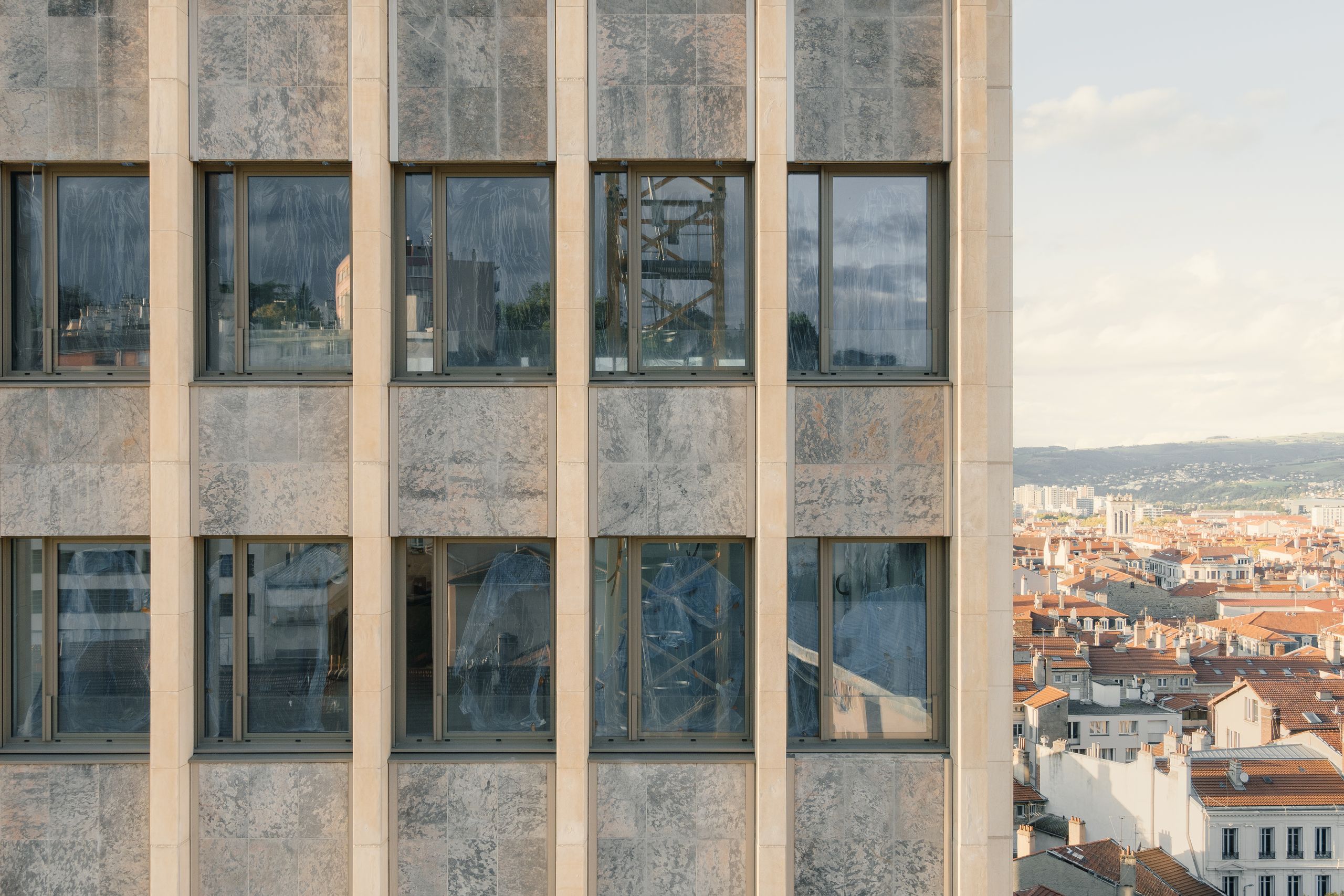 Façade rythmée de l’ancien IGH Émile Loubet en réhabilitation à Saint-Étienne, trame béton-pierre et baies vitrées ouvrant sur le paysage urbain en contrebas.