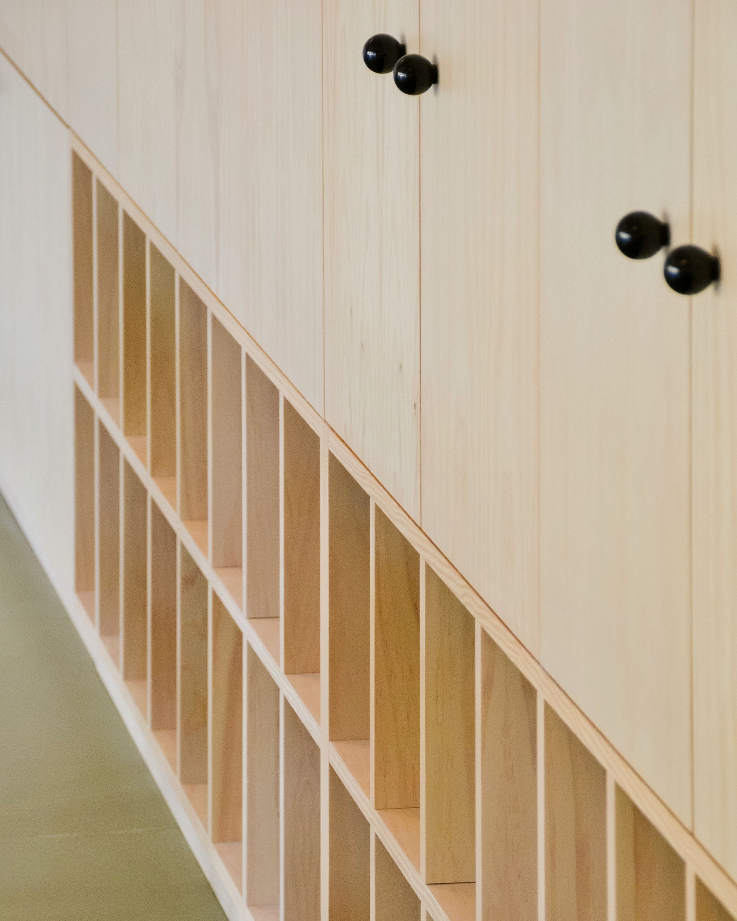 Détail d’un mobilier en bois du groupe scolaire du Bouchet à Bonneville, avec casiers ouverts en partie basse et portes pleines à poignées noires en partie haute.