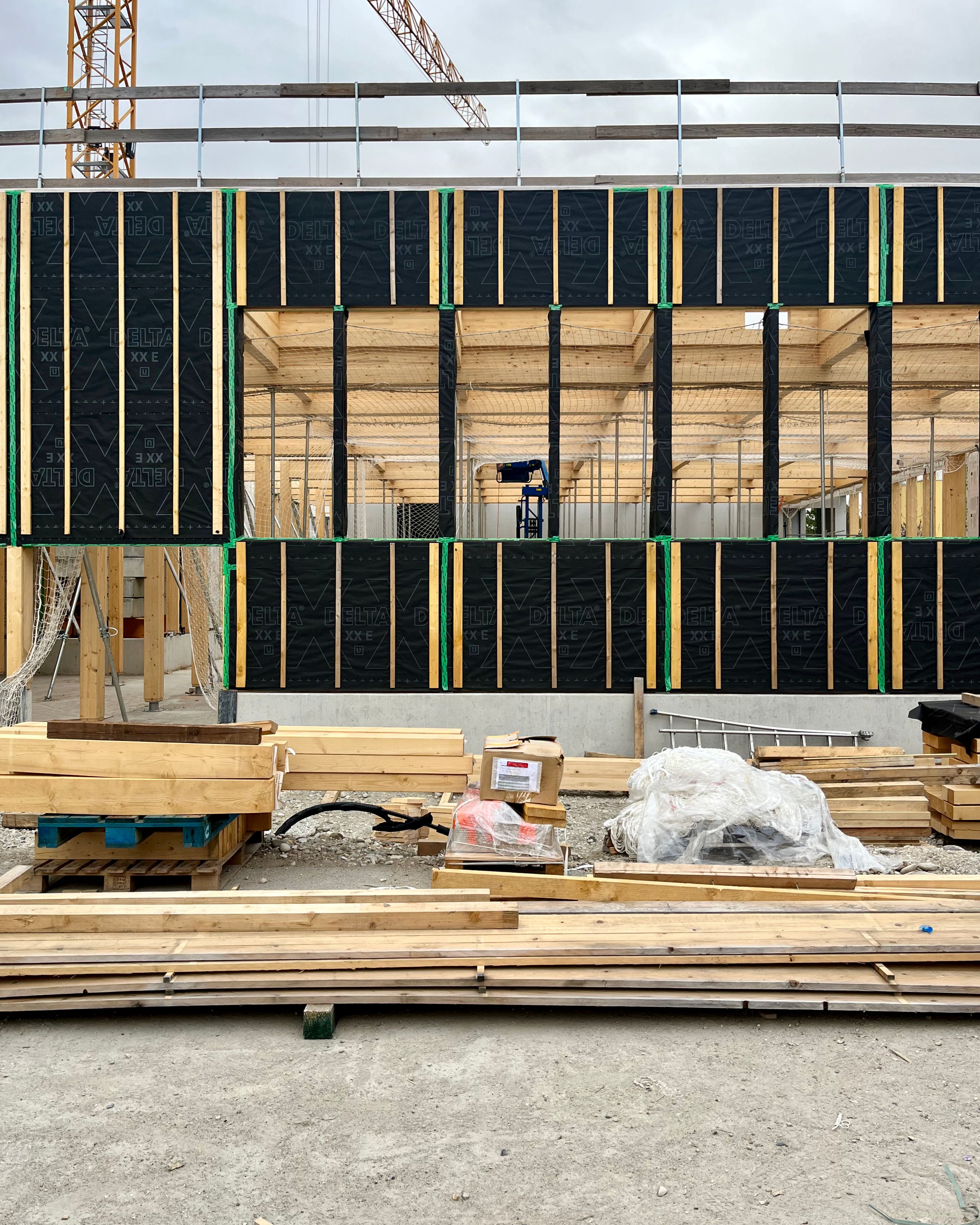 Chantier de la Cité campus Assia Djebar à Vaulx-en-Velin, structure bois apparente, trame régulière et façade en cours d’isolation, matériaux stockés au sol.