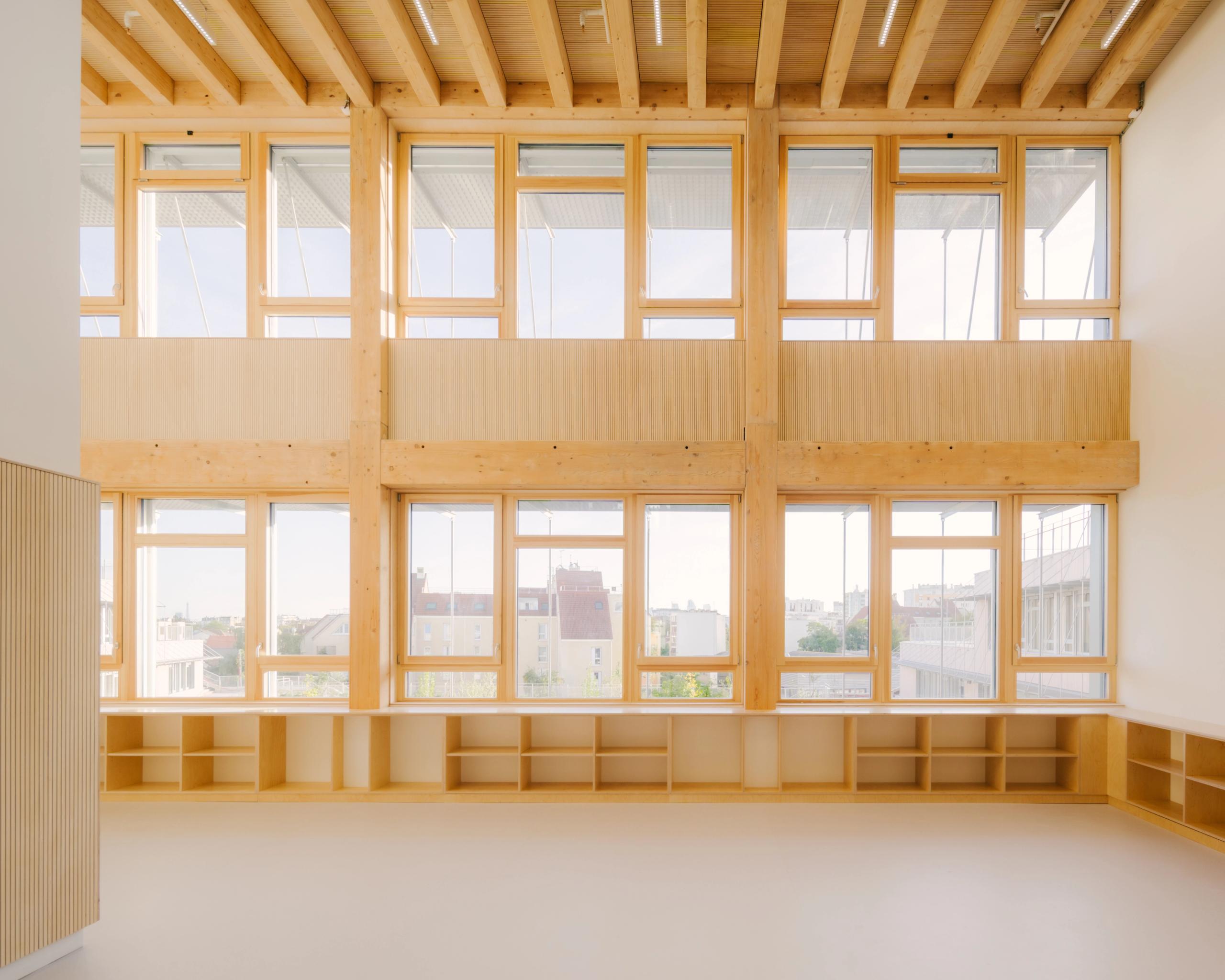 Intérieur du Groupe scolaire Dominique Frelaut à Colombes : grande salle traversante en structure bois, façade vitrée double hauteur ouvrant des vues sur la ville.