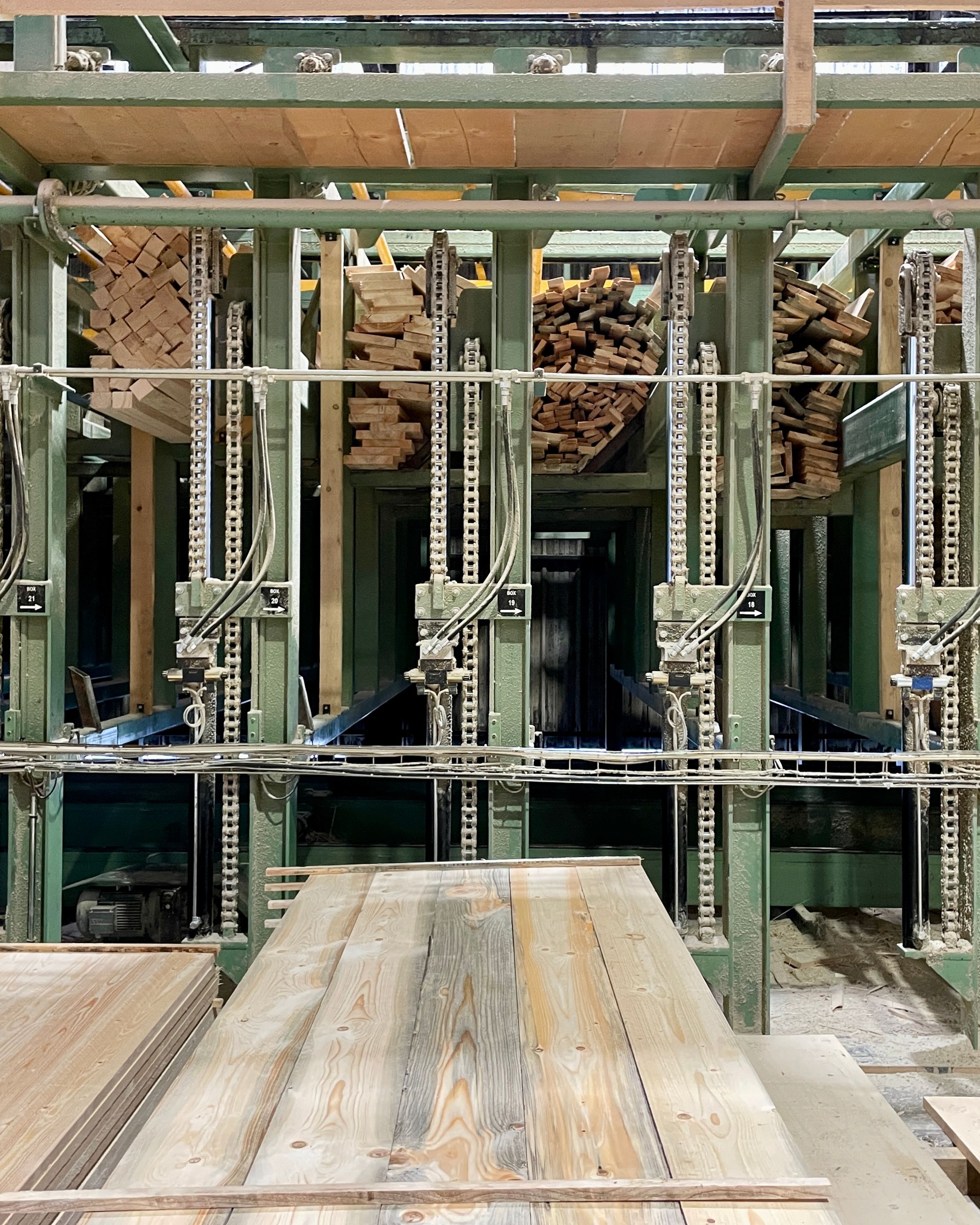 Processus de préfabrication bois pour le groupe scolaire Louis Pergaud à Levier, montrant stockage et tri mécanisé de planches en bois scolyté.