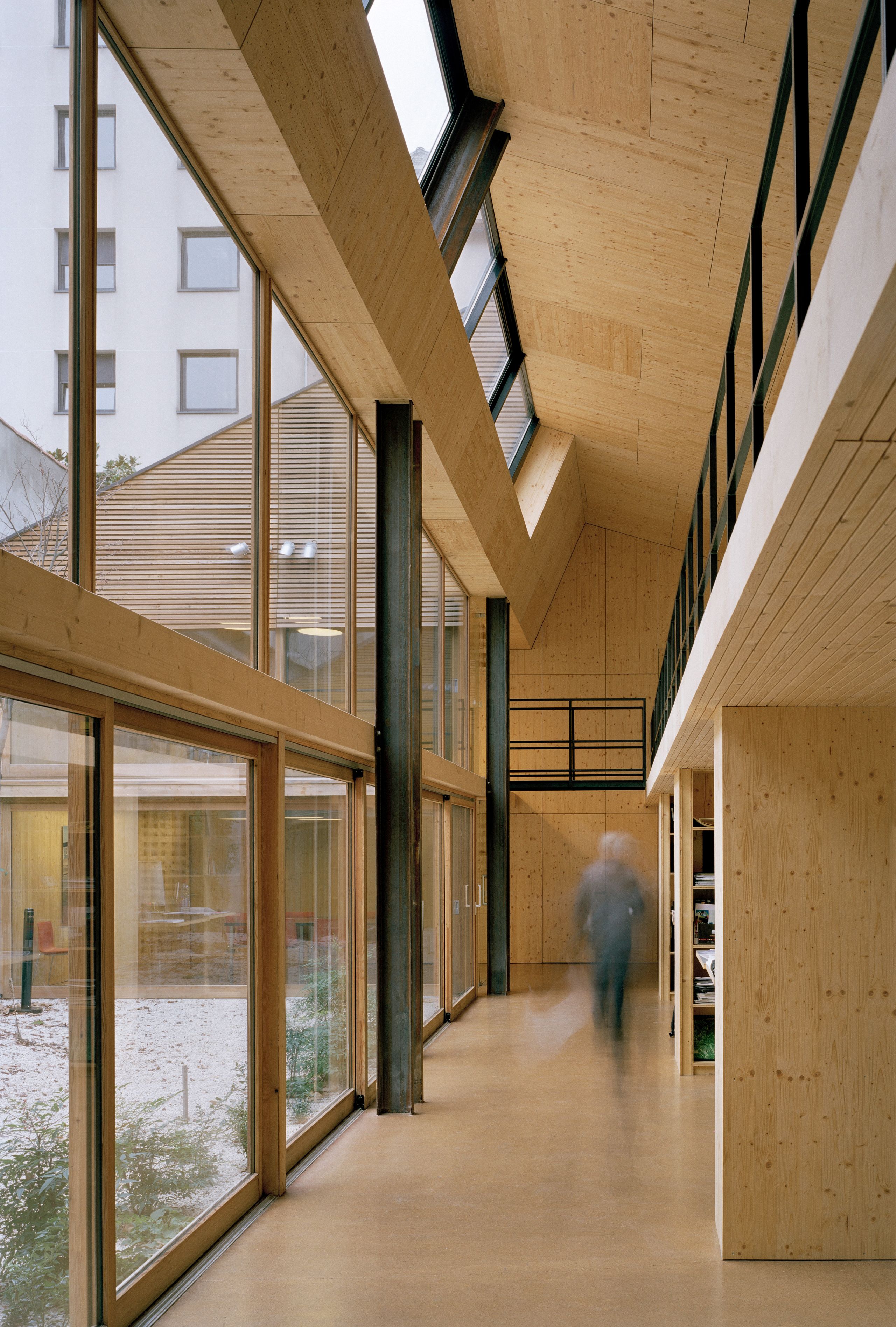 Couloir du local réhabilité à Lyon par Tectoniques, structure bois et acier, grande façade vitrée sur patio central, mezzanine ouverte et lumière nord homogène.