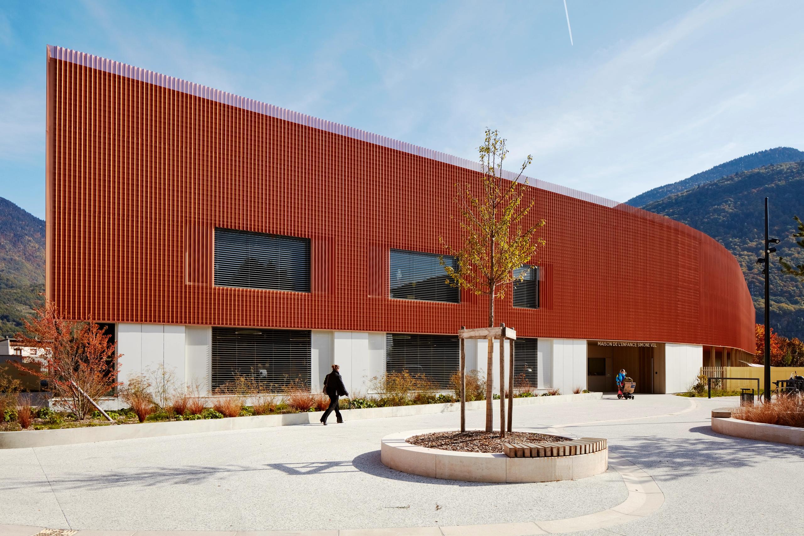 Simone Veil Early Childhood Center in Albertville, with a copper-toned perforated metal facade over a white base, large horizontal windows and a landscaped forecourt.