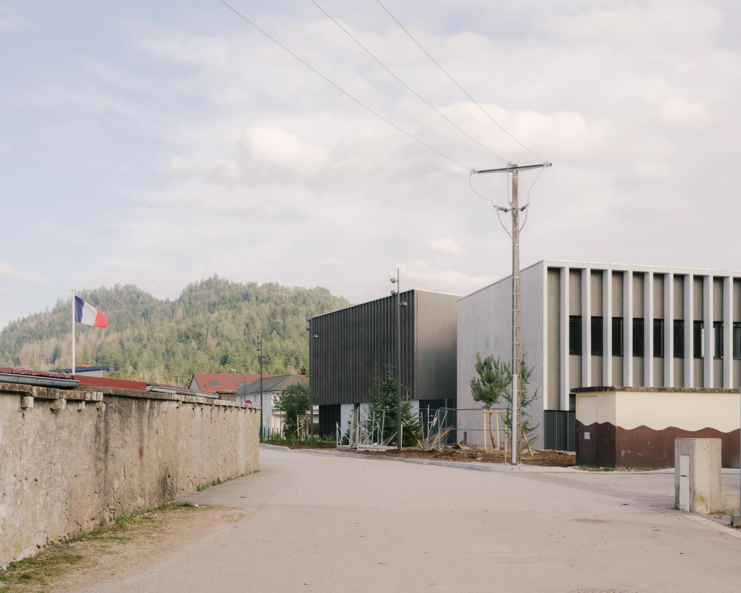 Vue de la façade du Collège du Ban à Vagney : volumes en peigne bois-béton, portique rythmé de lames verticales, inséré dans le paysage forestier vosgien.
