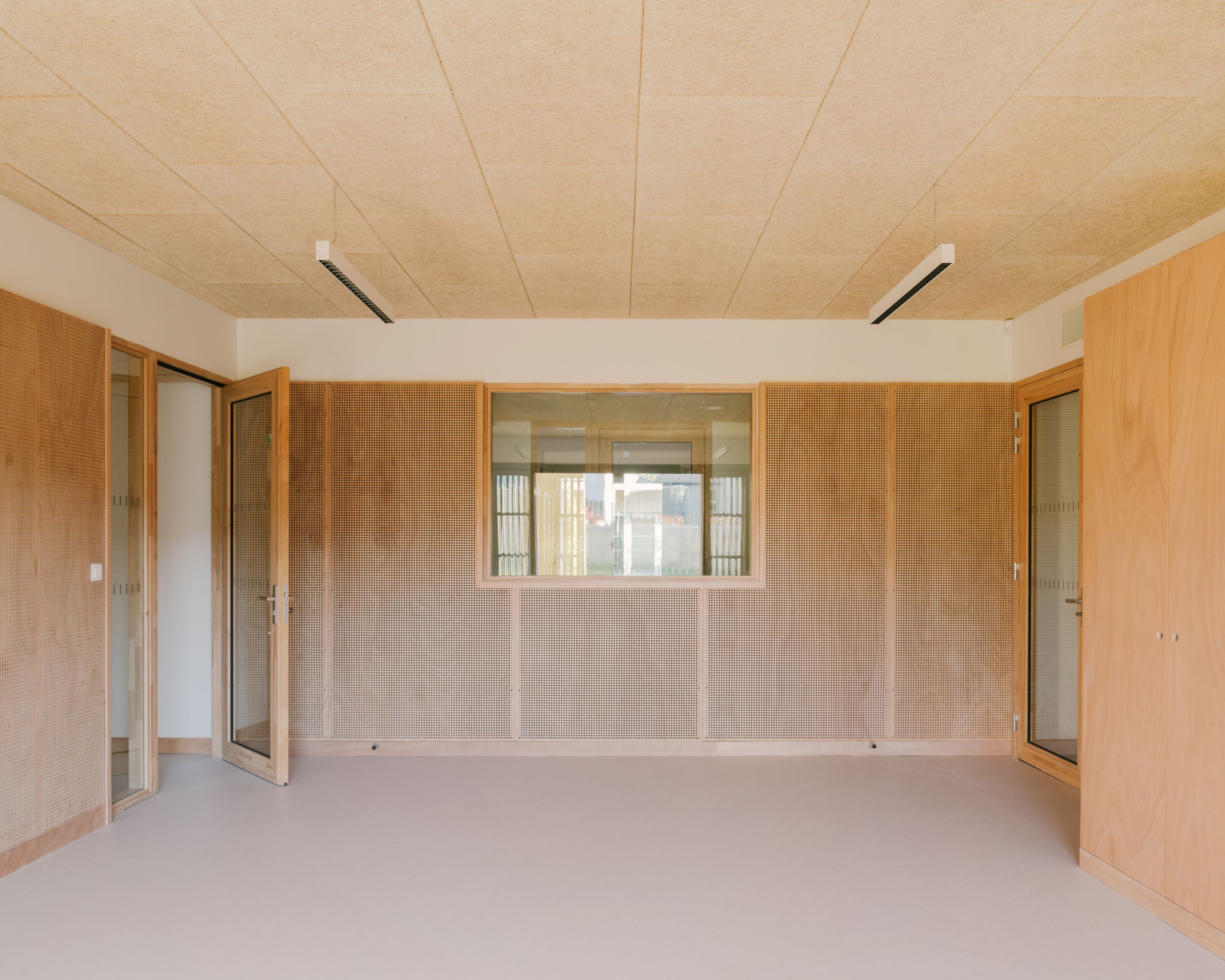 Intérieur du Pôle culture et jeunesse à Vaison-la-Romaine : salle claire aux parois bois perforé, menuiseries vitrées et plafond acoustique continu.