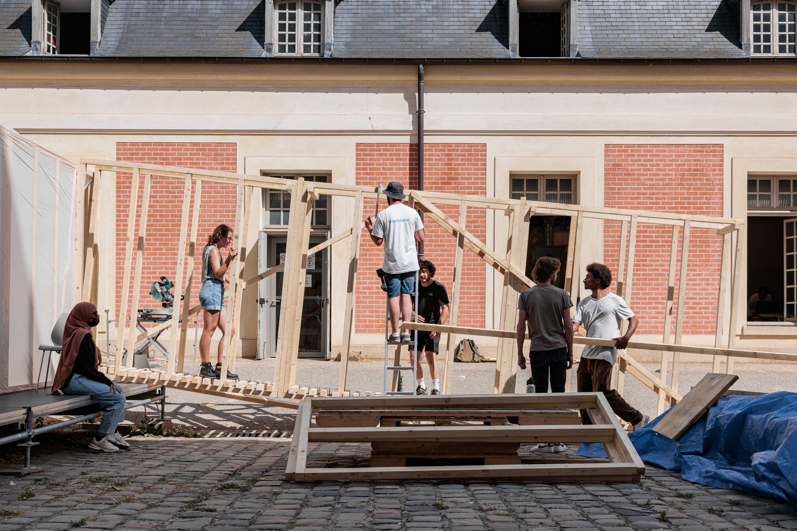 Montage in situ de la structure bois 60x60 du workshop à la Cour de la Maréchalerie, Versailles, formant un parcours ouvert devant les façades en briques.