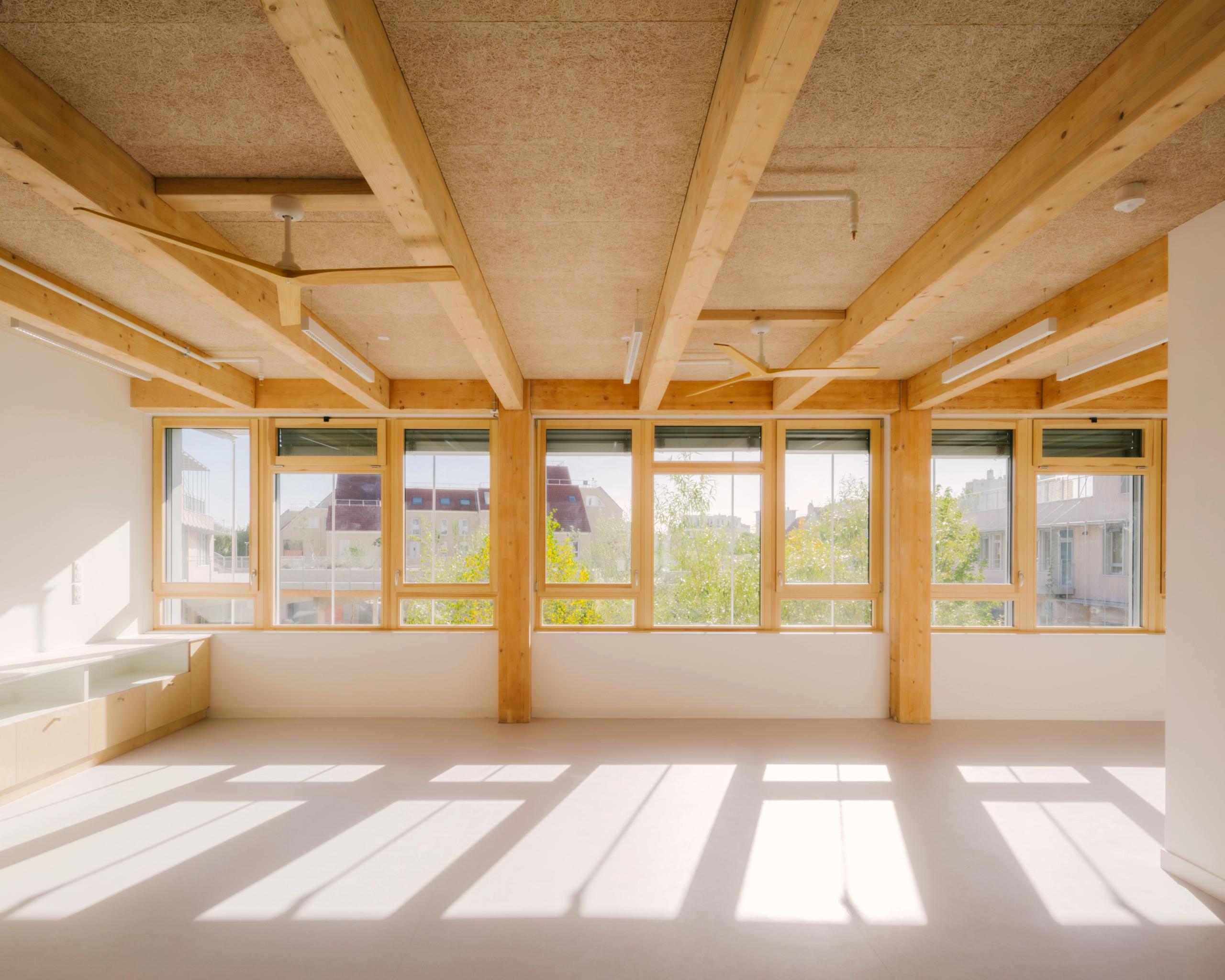 Salle de classe du Groupe scolaire Dominique Frelaut à Colombes, structure bois apparente, grandes baies vitrées sur la ville et lumière naturelle abondante.