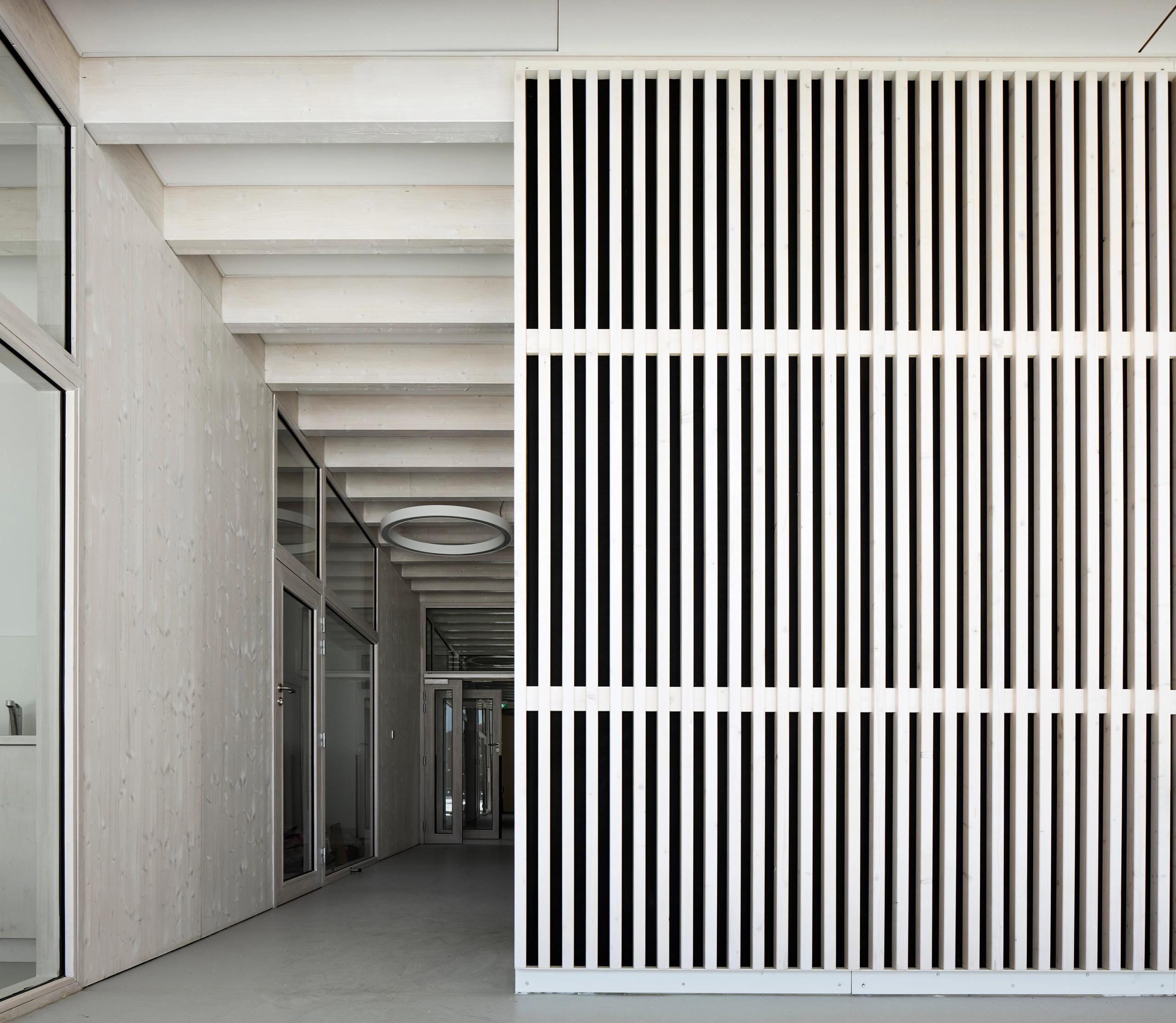 Maison de l’Enfance Simone Veil à Albertville : galerie intérieure en bois apparent, façade filtre à lames verticales blanches, lumière naturelle tamisée.