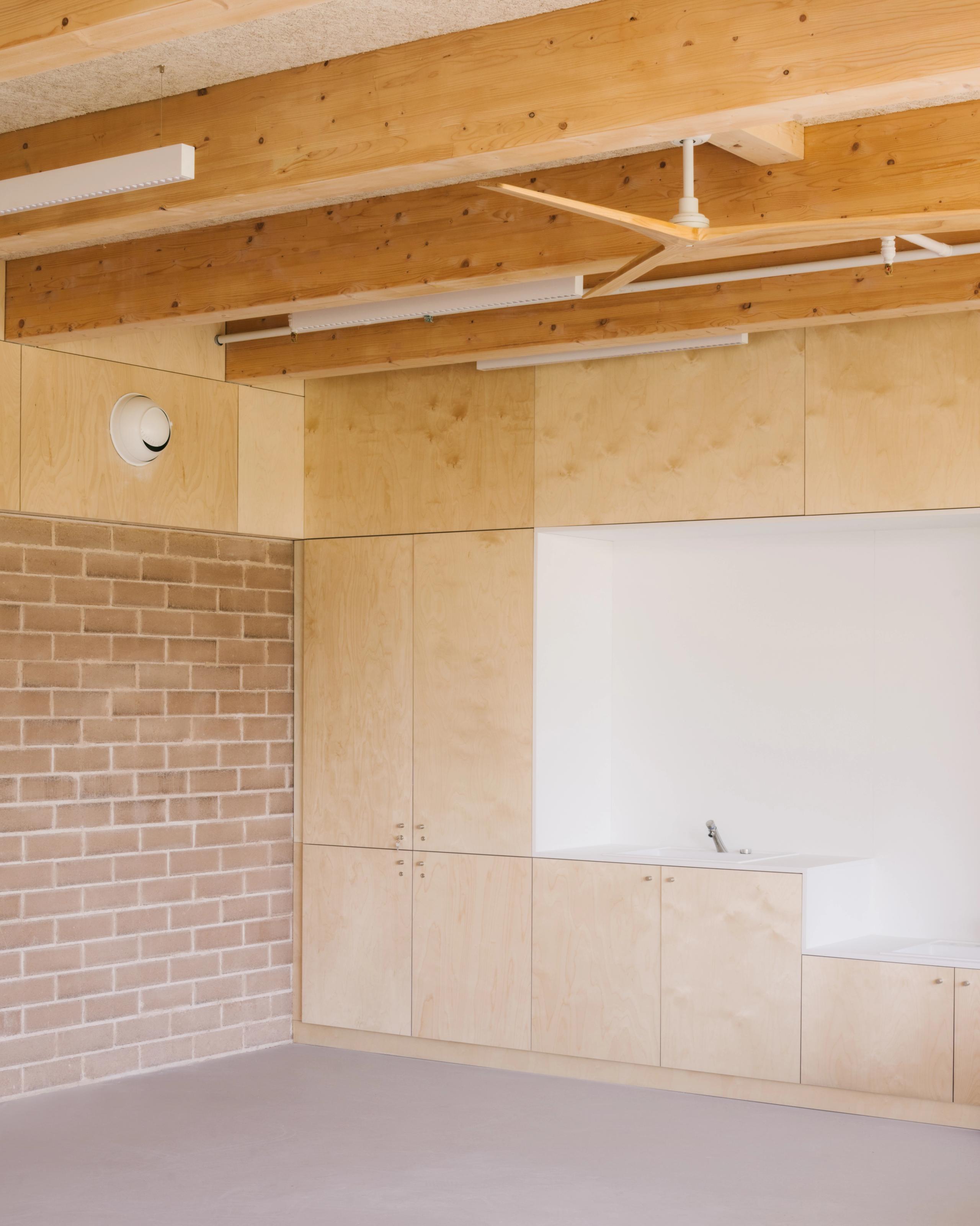 Intérieur du groupe scolaire Dominique Frelaut à Colombes : salle claire avec structure bois apparente, mur en brique, rangements intégrés et point d’eau.