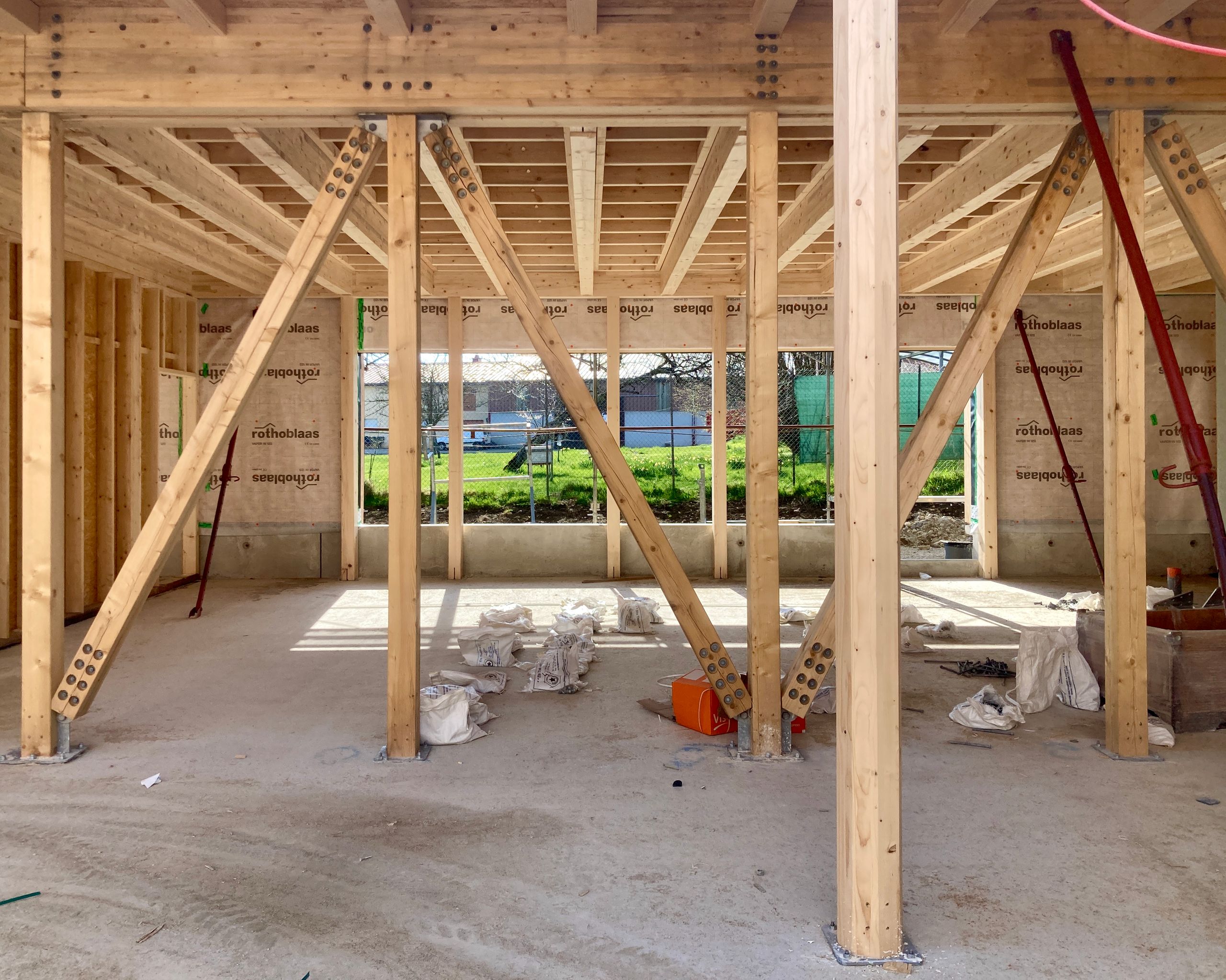 Structure bois en cours de chantier du groupe scolaire Louis Pergaud à Levier, poteaux et contreventements apparents, ouvrant sur la future cour paysagée.