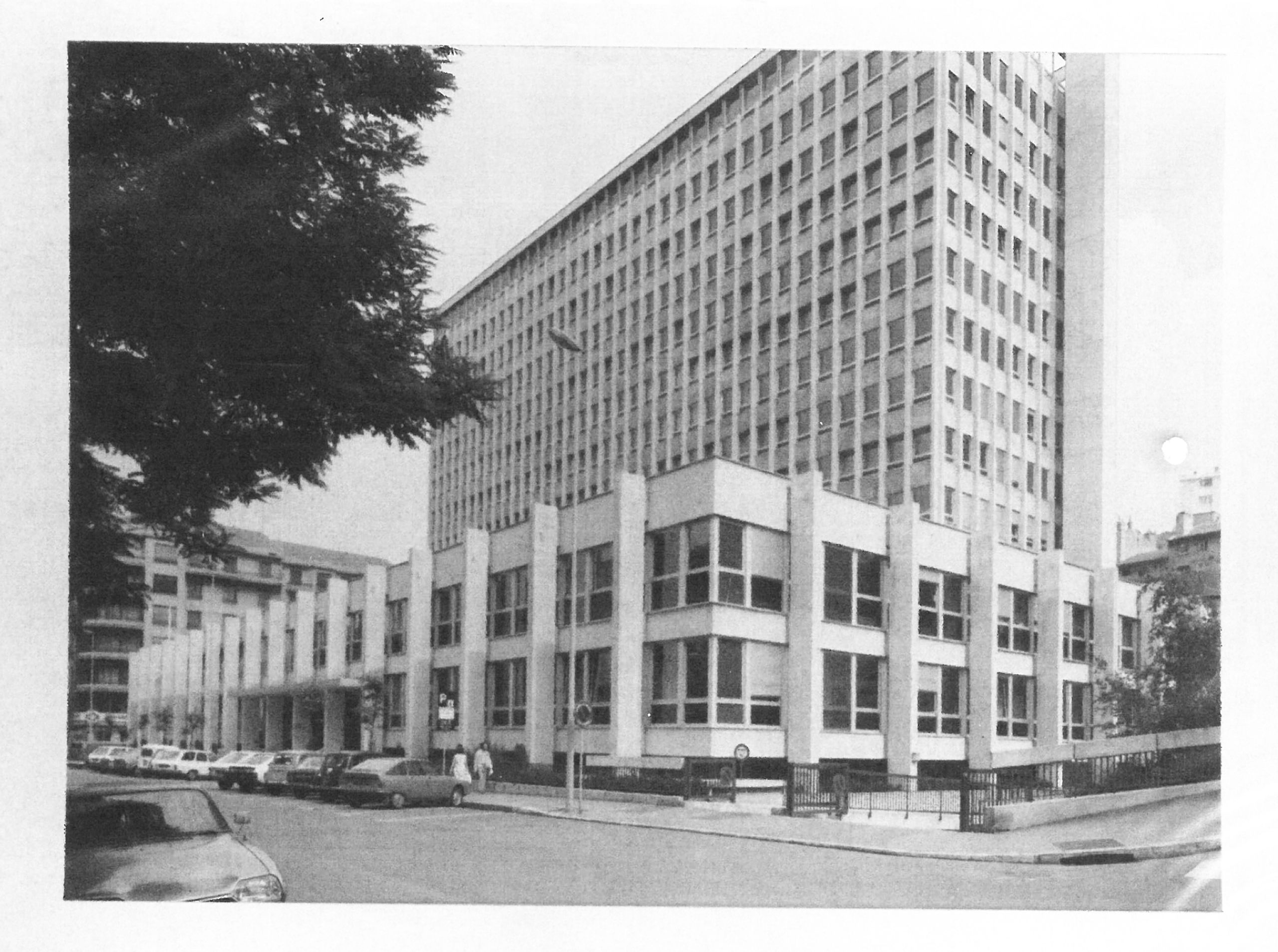 Vue de l’ancien IGH Émile Loubet à Saint-Étienne : socle bas rythmé de portiques en béton et tour de bureaux vitrée, implantés en angle sur rue.
