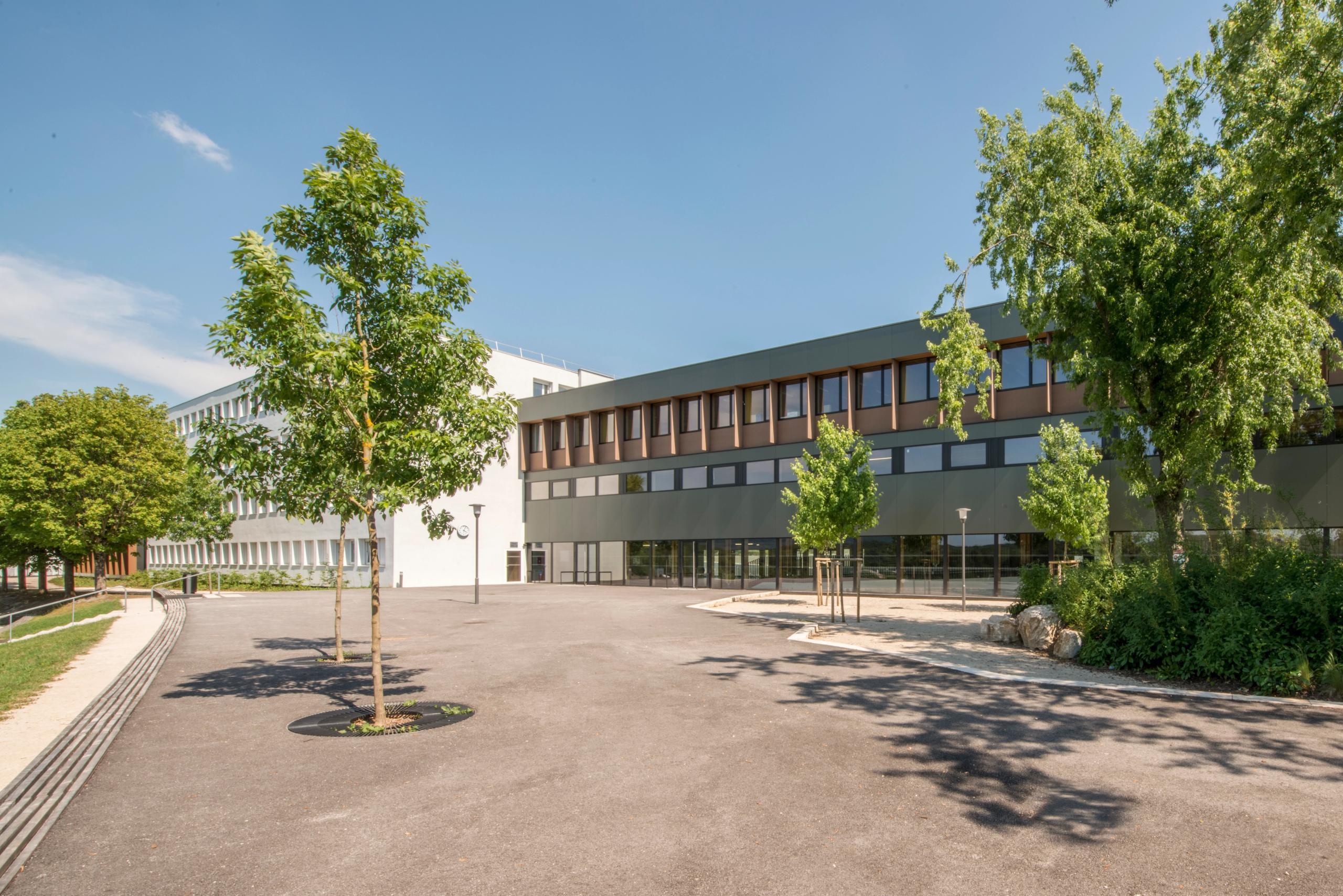 Façade rénovée du collège Pierre-Joseph Proudhon à Besançon, externat blanc et extension bois sombre encadrant une vaste cour minérale plantée.