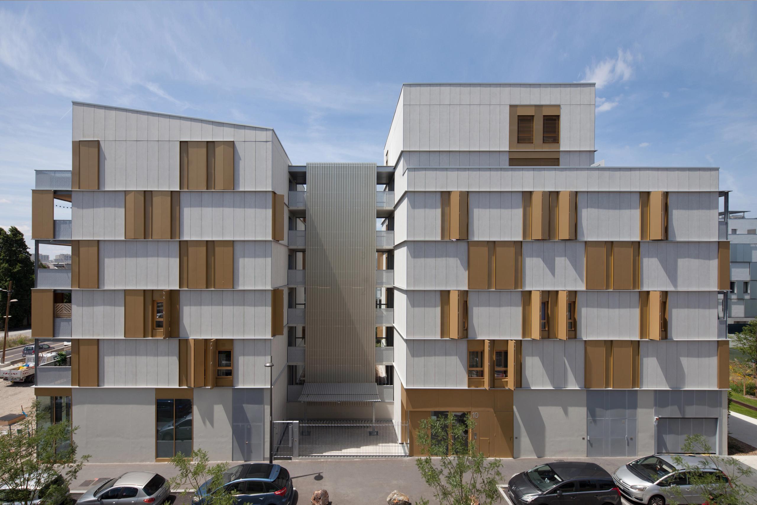 Façade des 55 logements Tectoniques à Lyon : deux volumes en béton et métal, ossature bois, volets coulissants dorés et faille centrale desservant les circulations.