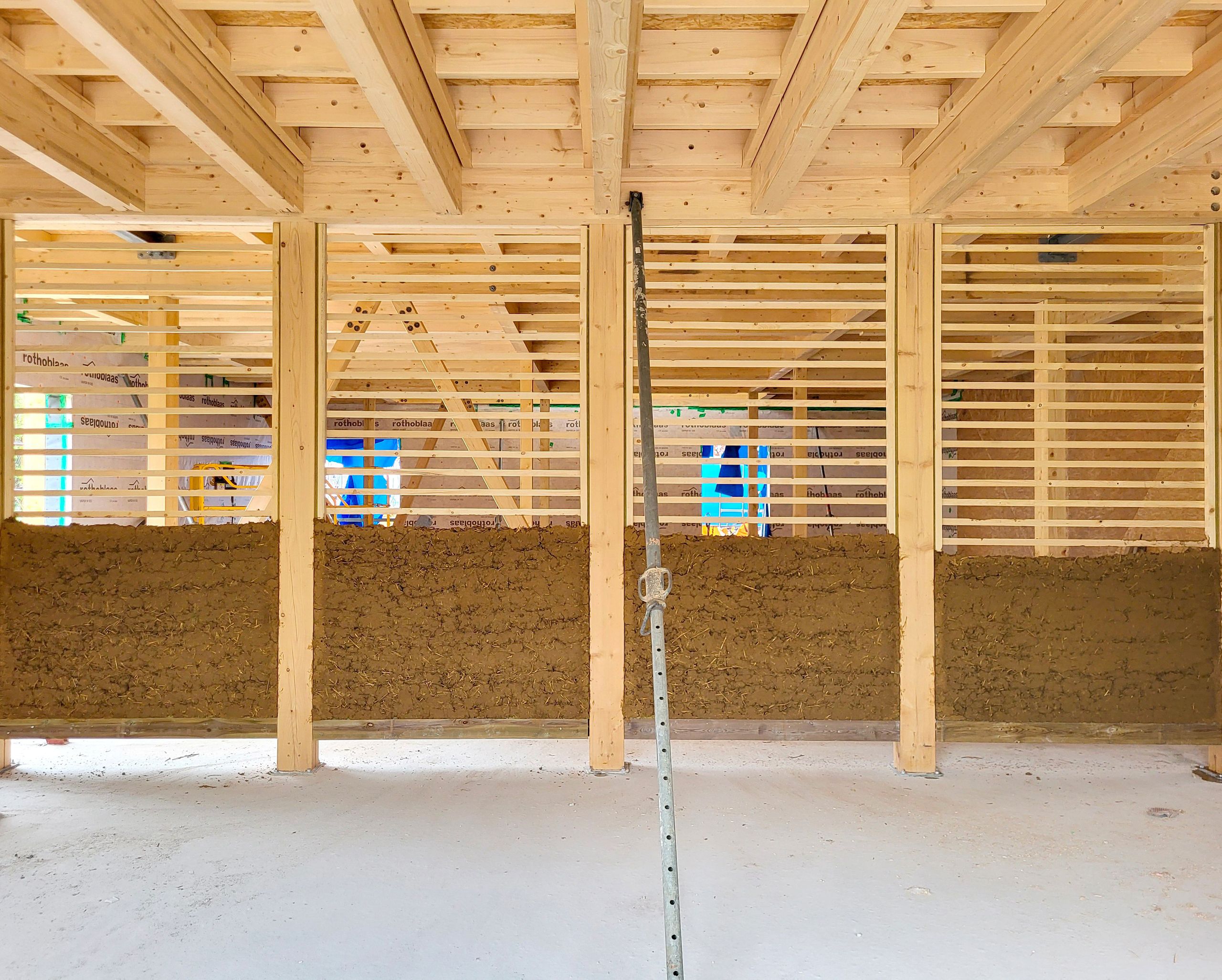 Chantier du groupe scolaire Louis Pergaud à Levier : structure bois apparente, remplissage en cob entre montants et lames horizontales, plancher bas béton lisse.