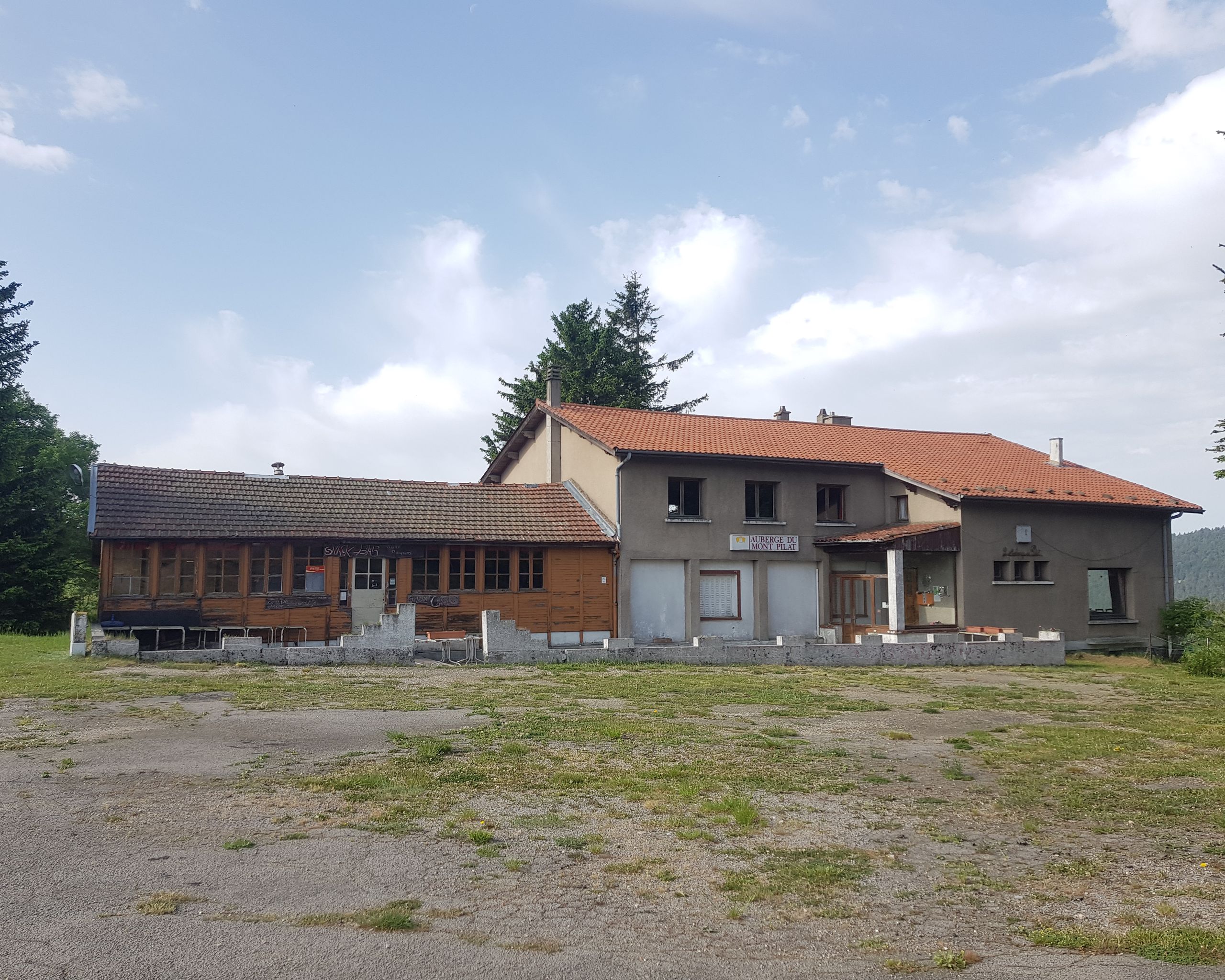 Vue de l’ancienne auberge de montagne du col de l’Oeillon à Véranne, volumes bas en maçonnerie et bois sous toitures tuiles, en lisière de clairière.