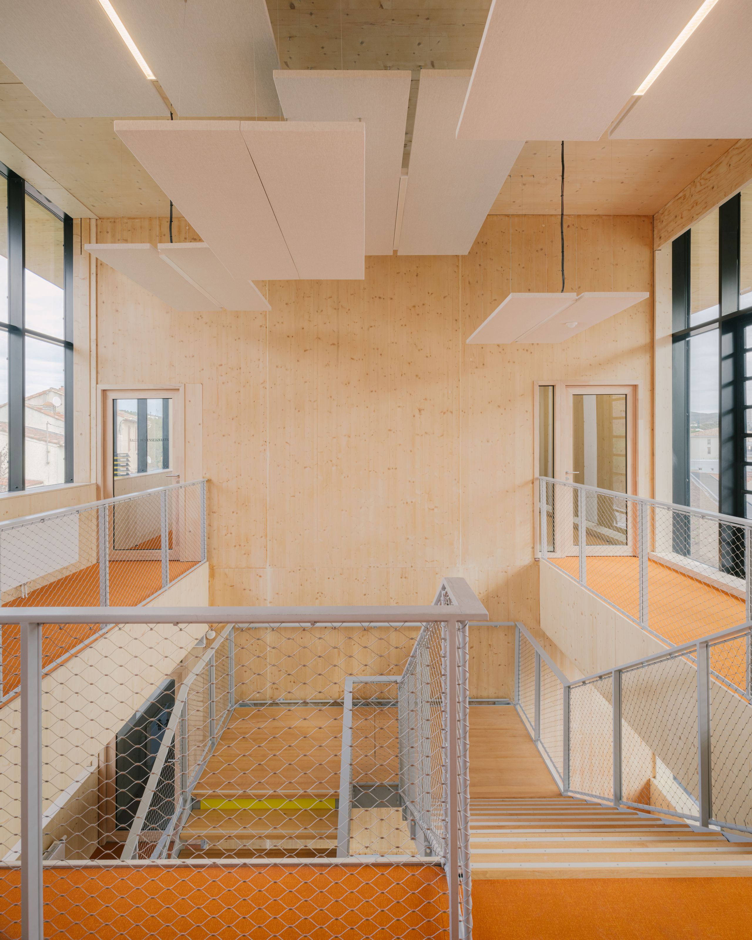 Circulation intérieure de la médiathèque et School complex Claudie Haigneré aux Pennes-Mirabeau, escalier bois, garde-corps métal et panneaux acoustiques suspendus.