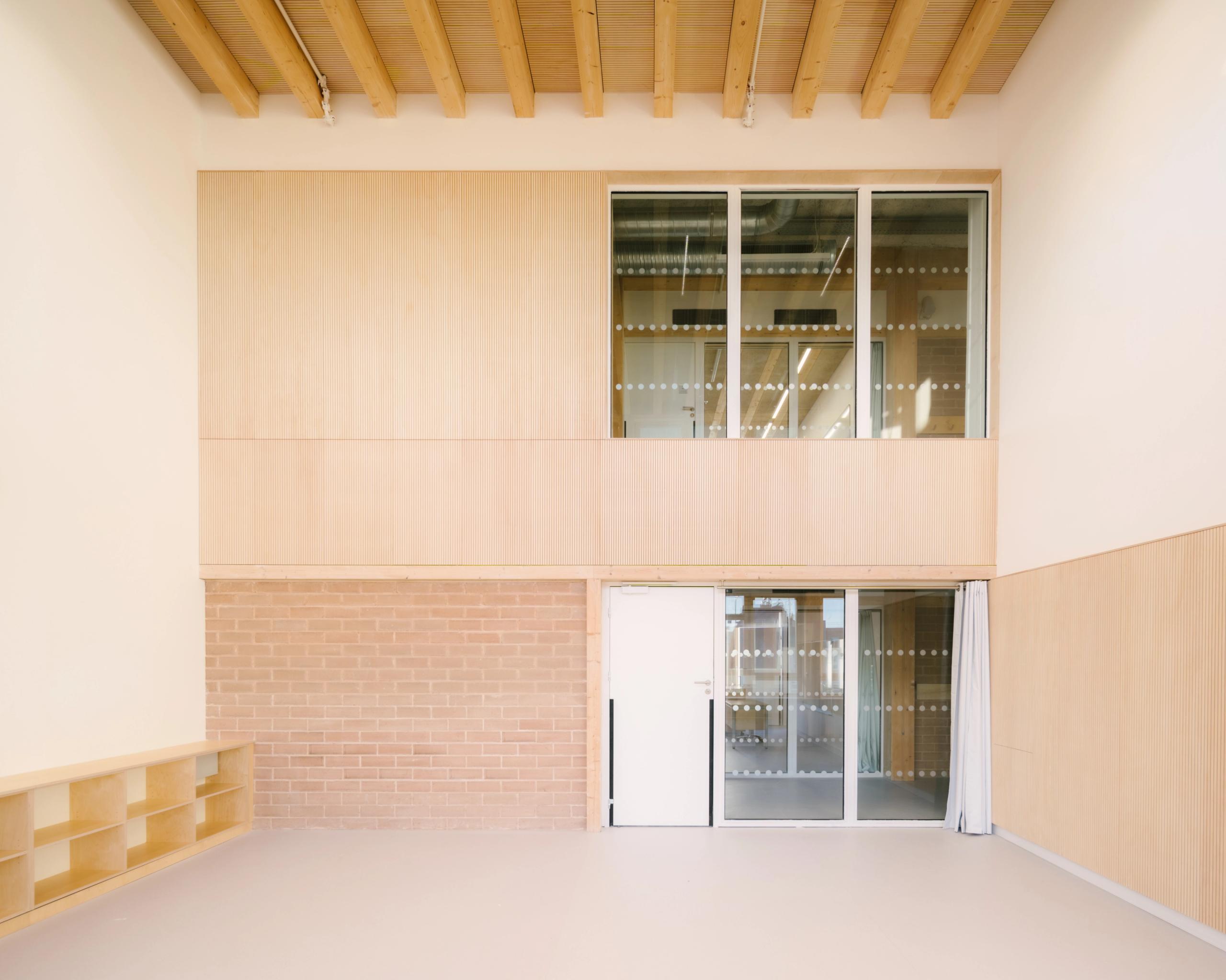 Intérieur du groupe scolaire Dominique Frelaut à Colombes, grand volume clair en bois et brique, façade intérieure vitrée sous plafond à poutres apparentes.