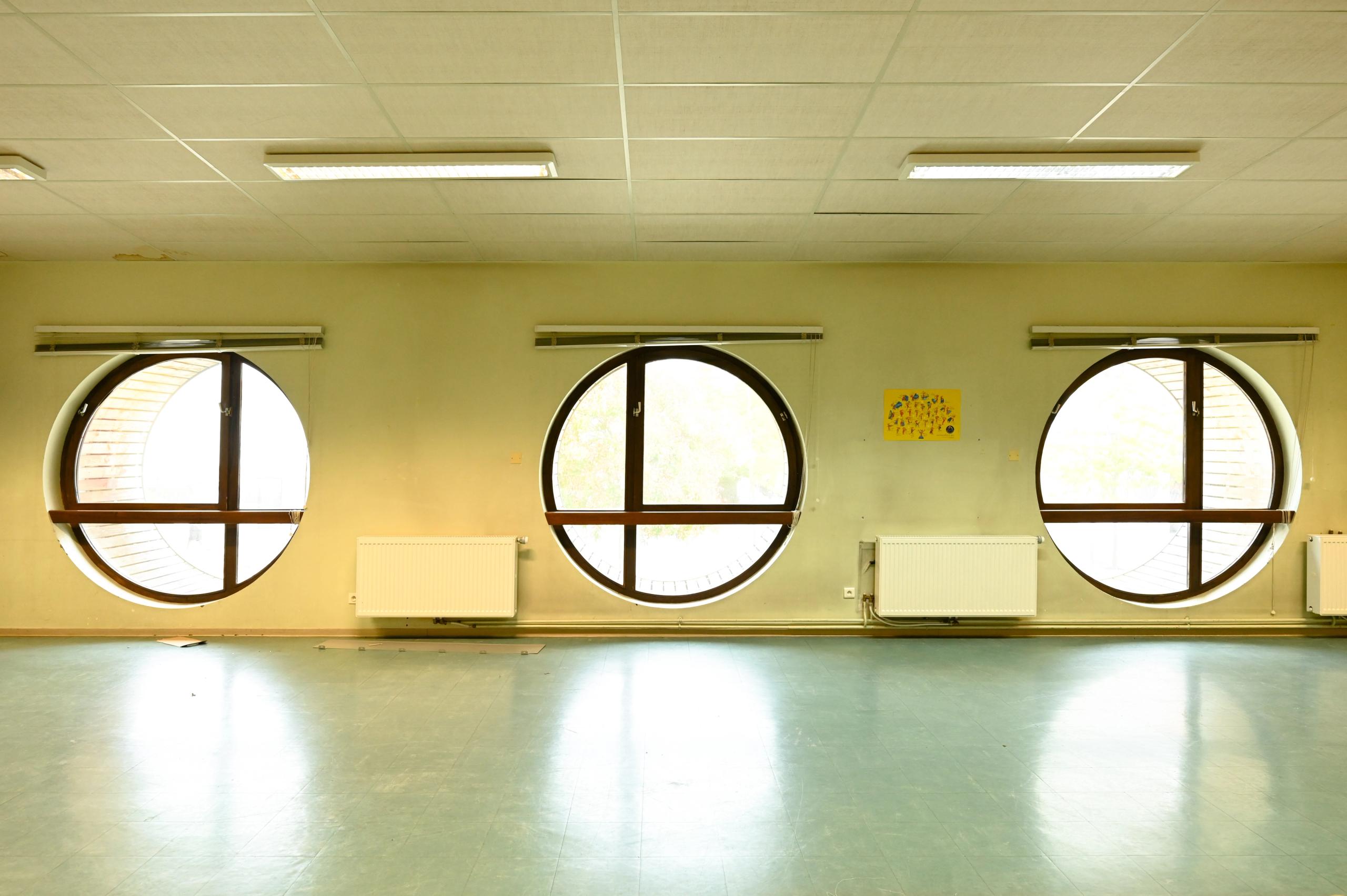 Etat existant du conservatoire intercommunal d’Annemasse : salle éclairée par trois baies circulaires, avec sol souple, radiateurs et plafond suspendu.