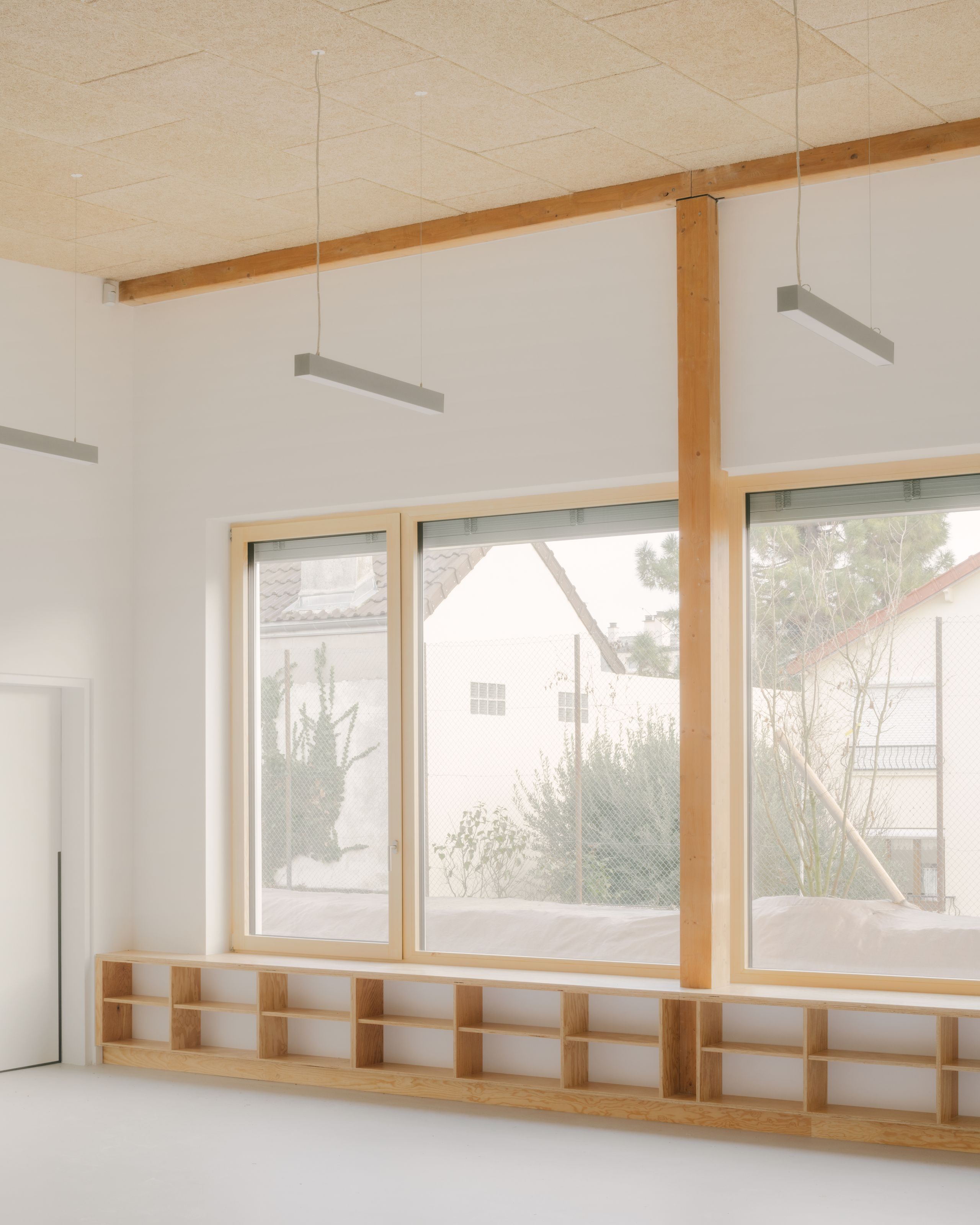 Intérieur d’une salle des groupes scolaires Jacqueline Auriol et Jean Jaurès au Bourget, avec structure bois apparente, grands vitrages et rangements bas intégrés.