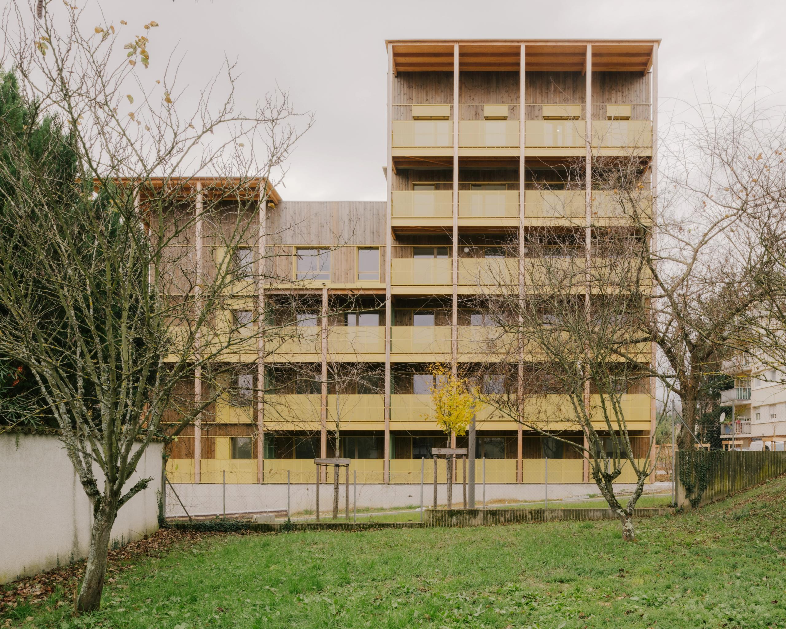Façade en paliers des 84 logements Tectoniques à Trévoux, structure bois et poteaux-dalles béton, coursives et balcons filants sur parc public.